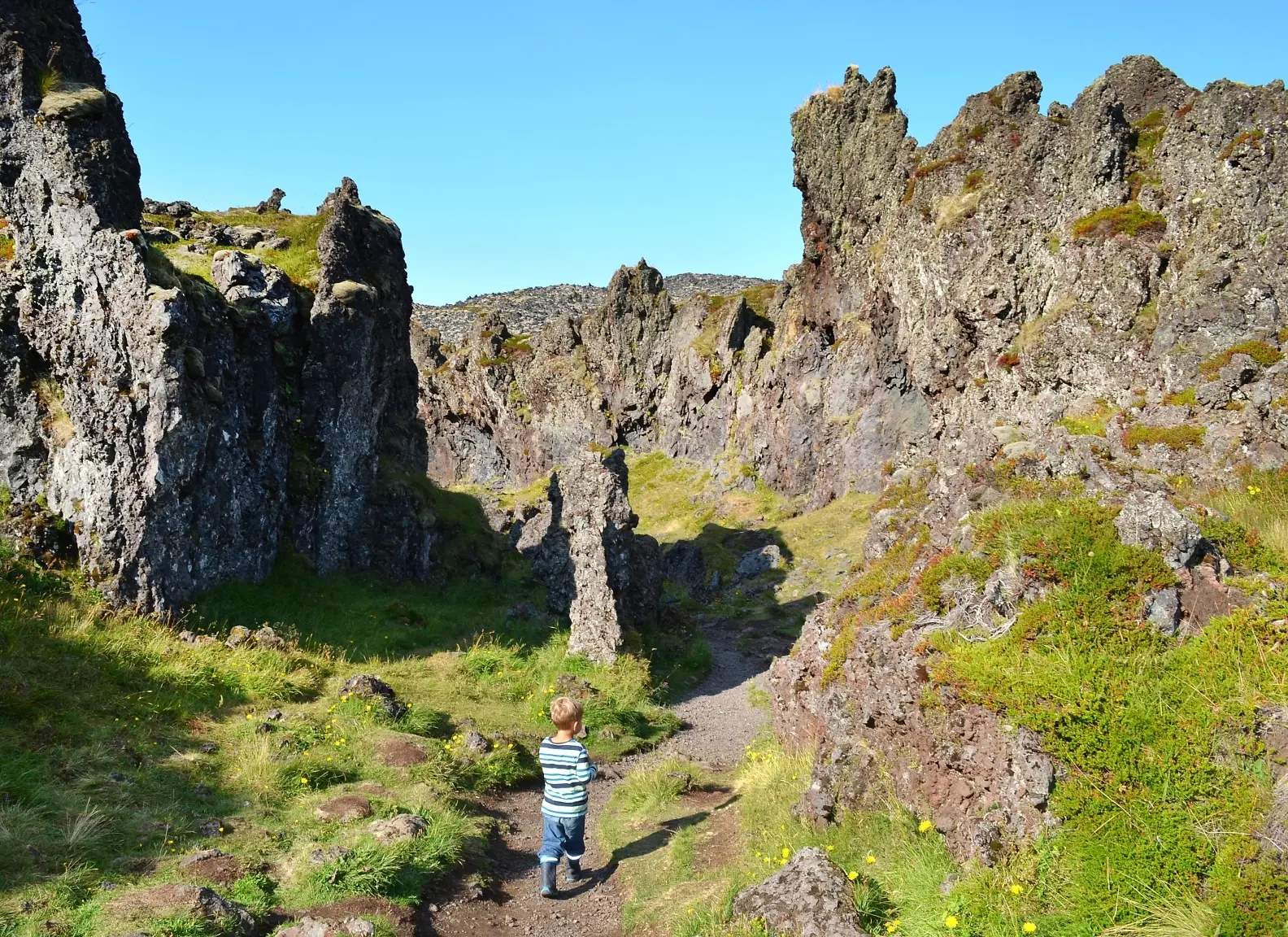 Kind steht vor einem riesigen Felsenlabyrinth in Snaefellsnes bei schönem blauen Himmel