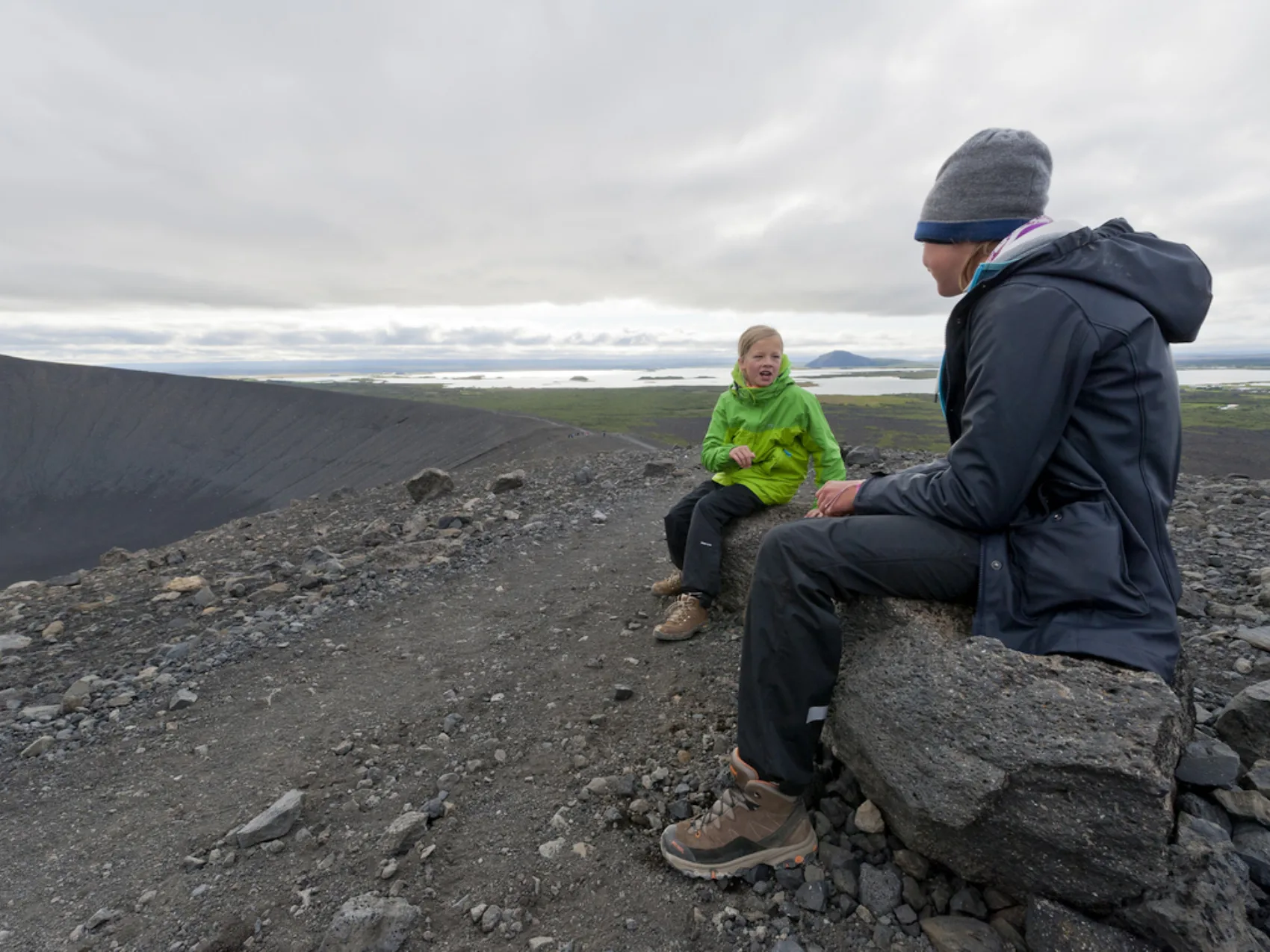 Zwei Kinder in Nordisland am Myvatn See, graue felsige Kraterlandschaft im Hintergrund