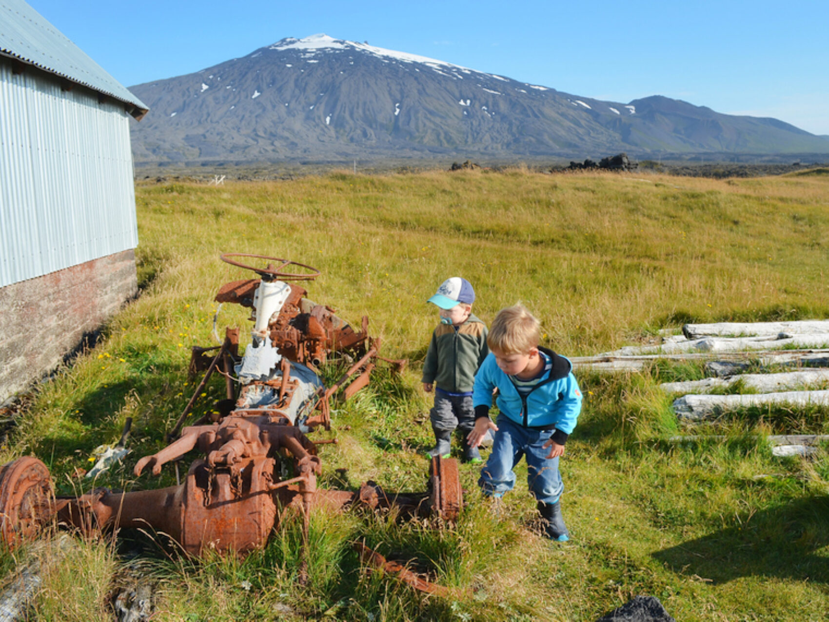 Kinder auf Schatzsuche vor den Füßen des Snaefellsjökull, alter verrosteter Traktor, Hintergrund Berg mit weißer Spitze, grüne Wiese