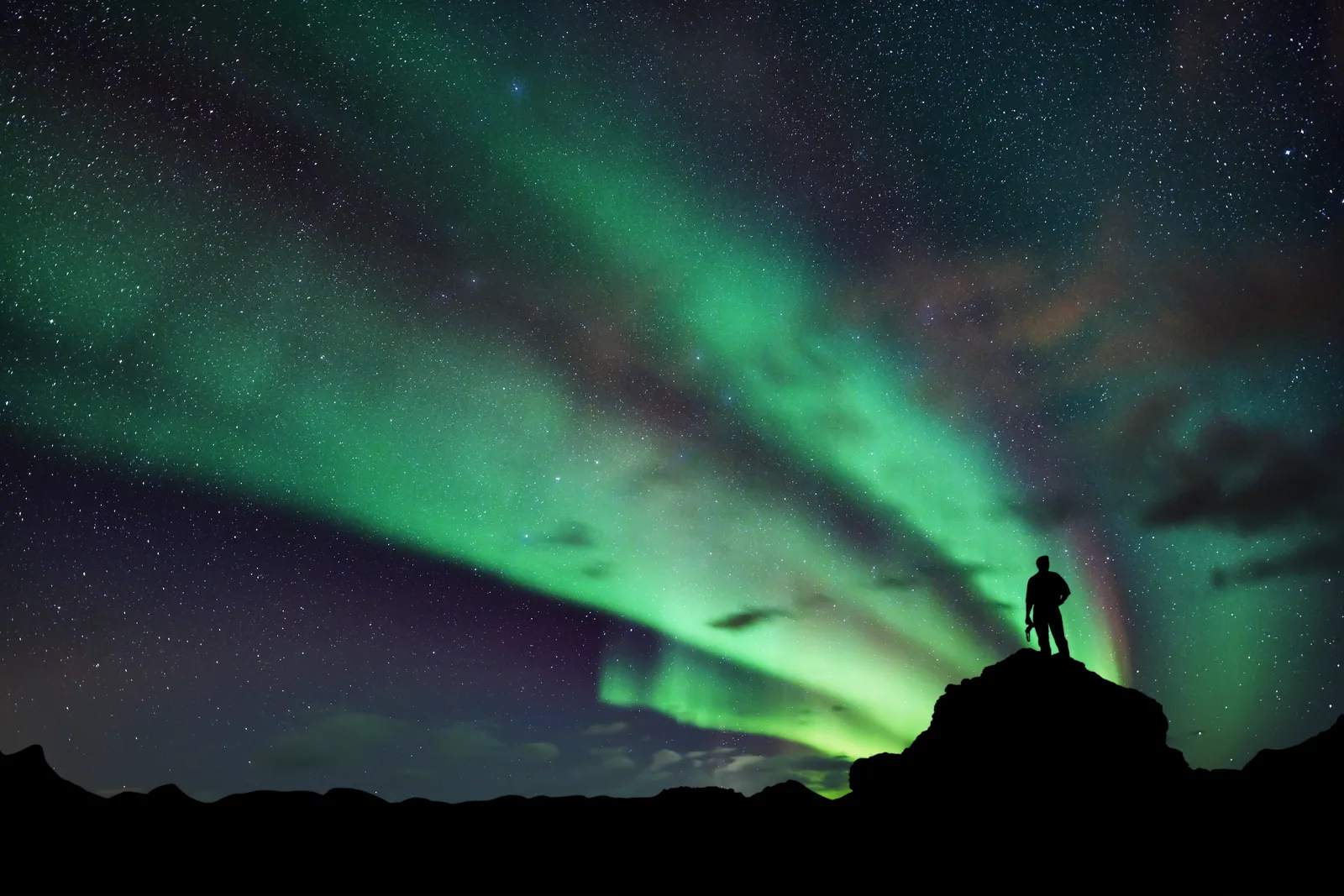 Ein Tourist steht auf einem Felsen und genießt die Nordlichter.