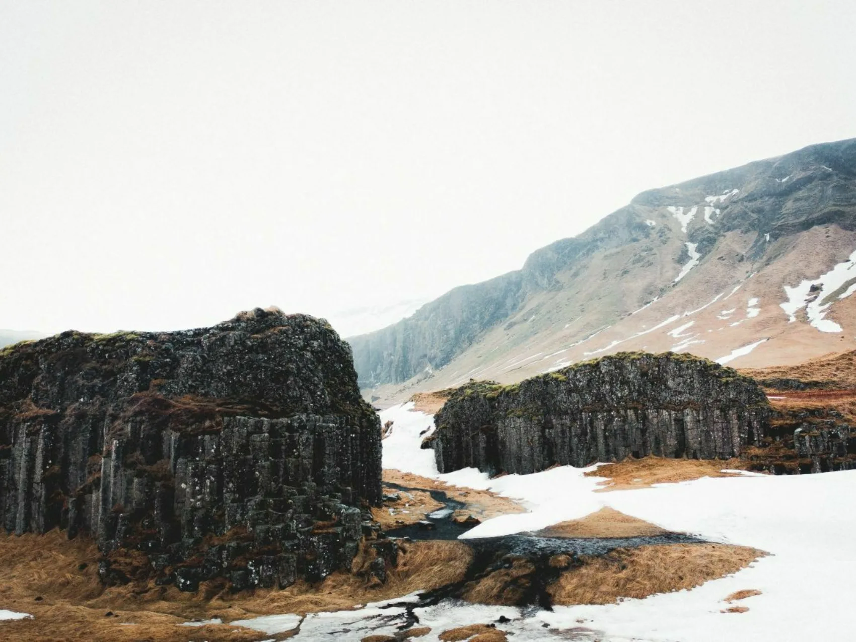 Südisland Dverghamrar Zwergklippenlandschaft mit Schneeflächen, vereinzelt braunes Gras, leichter Nebel im Hintergrund