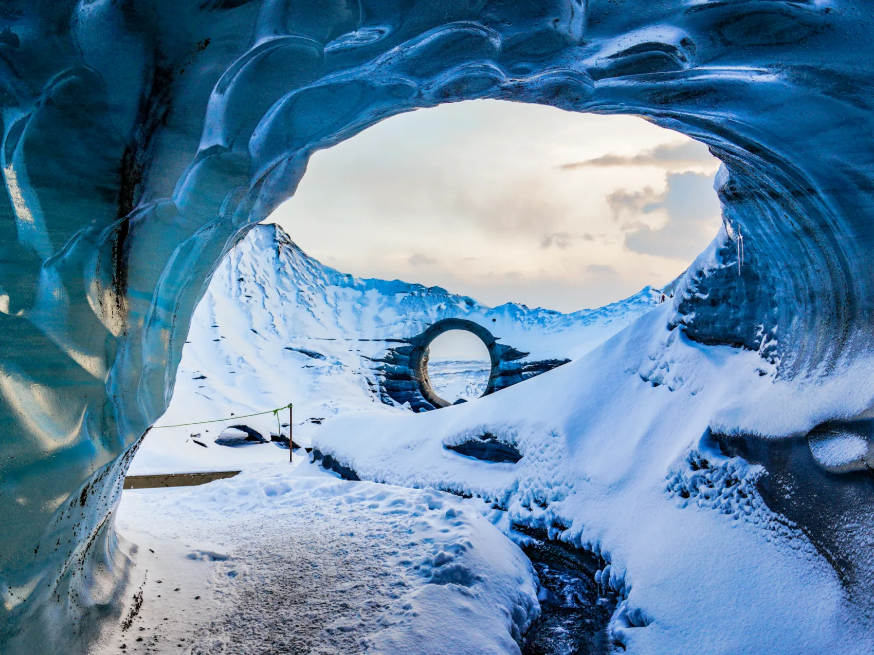 Blick aus einer Eishöhle über einen verschneiten Wanderweg.