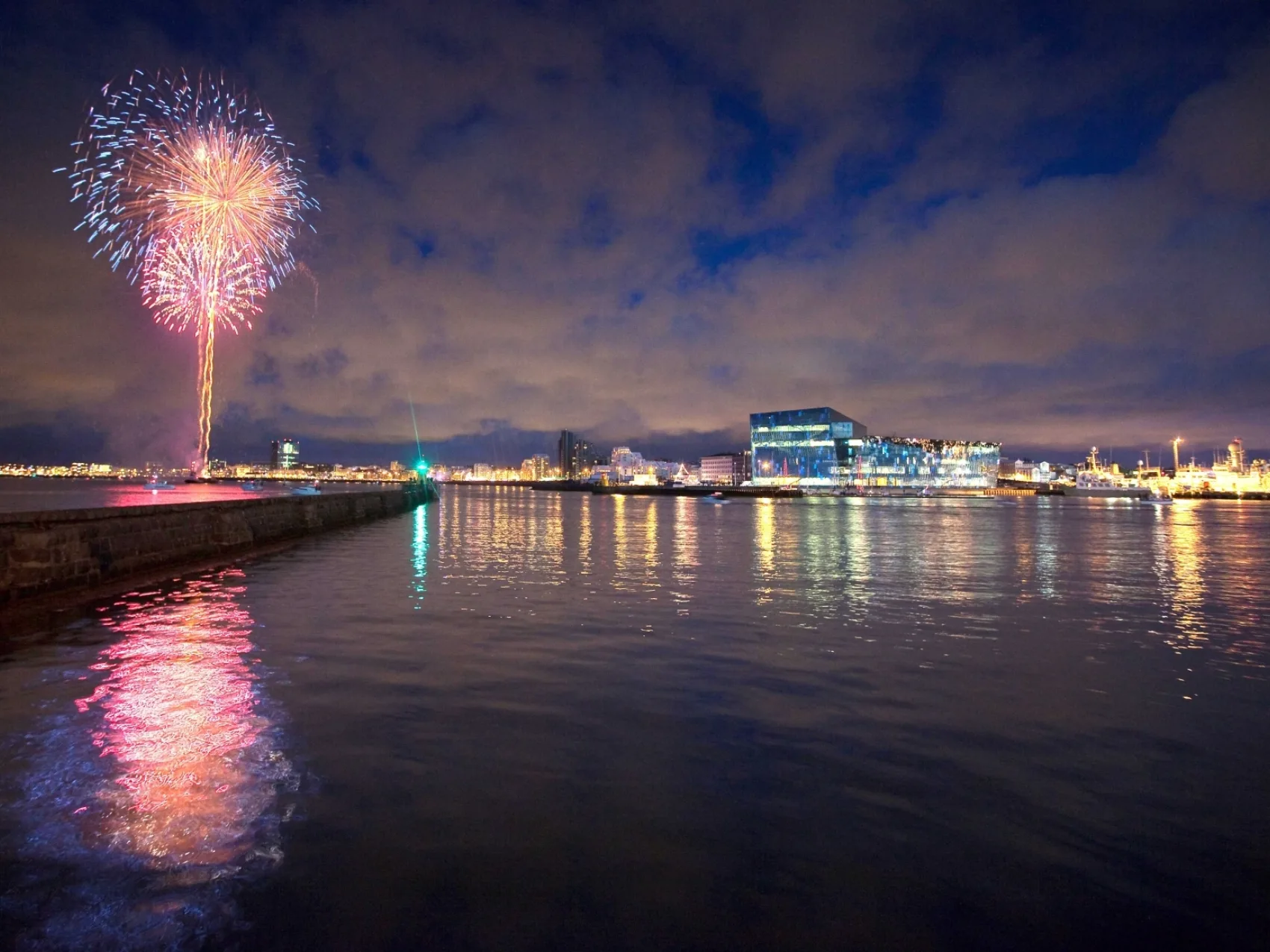 Silvester Reykjavik Harpa, Feuerwerk am Himmel, das sich im Wasser spiegelt. Lichter der Stadt und die Harpa am Horizont