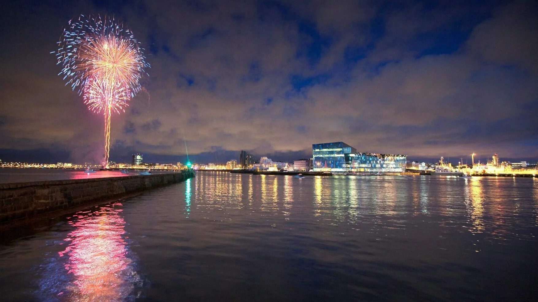 Silvester Reykjavik Harpa, Feuerwerk am Himmel, das sich im Wasser spiegelt. Lichter der Stadt und die Harpa am Horizont