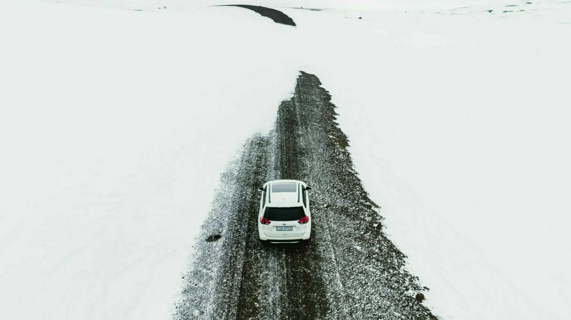 Straße mit Schnee in Westisland im Winter, weißes Auto fährt auf Straße, die Schneeverwehungen hat, rund um die Straße ist alles weiß