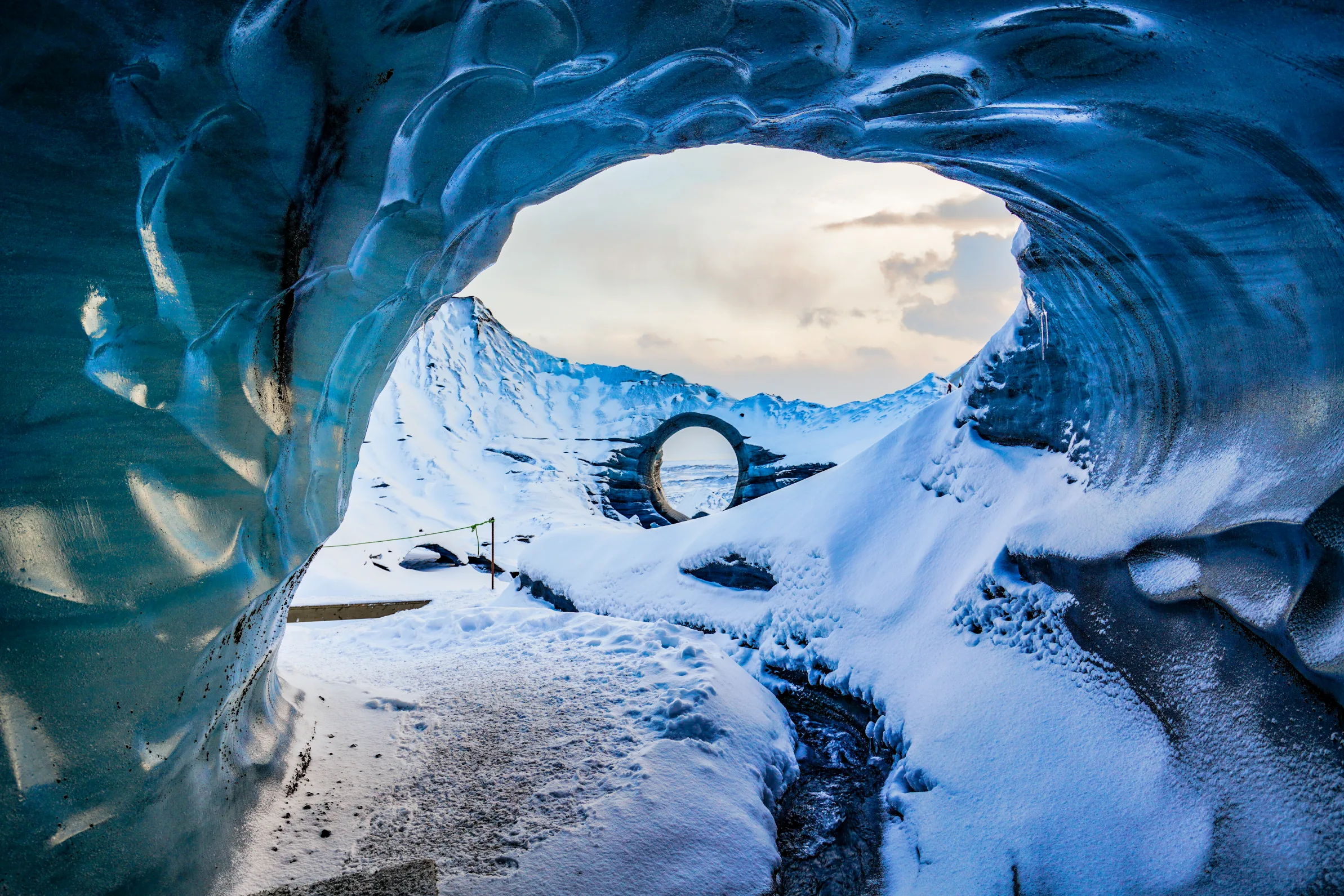 Blick aus einer Eishöhle über einen verschneiten Wanderweg.