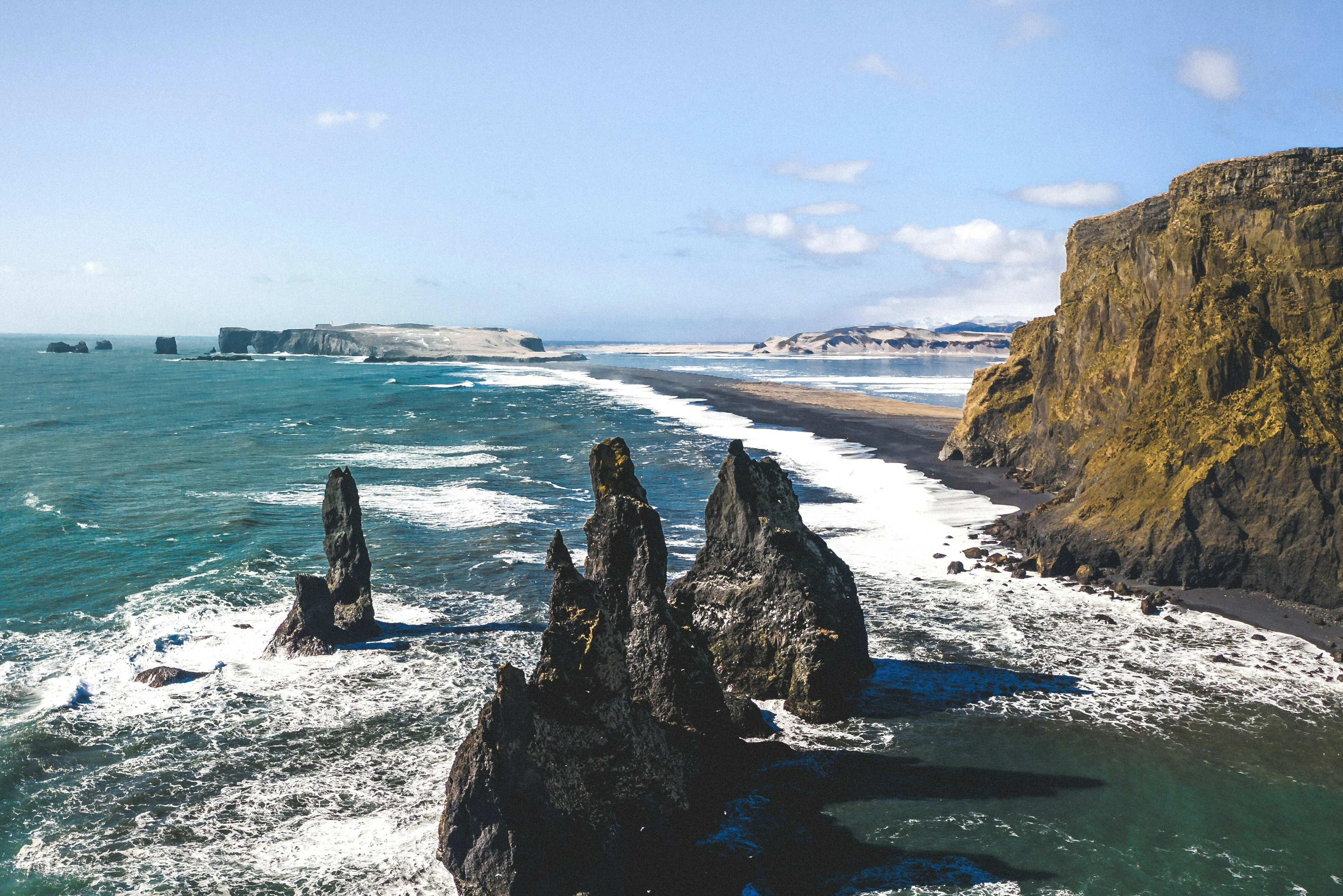 Eine farbenfrohe Strandlandschaft in Südisland mit schönen Klippen, klarem Himmel und Wellen.