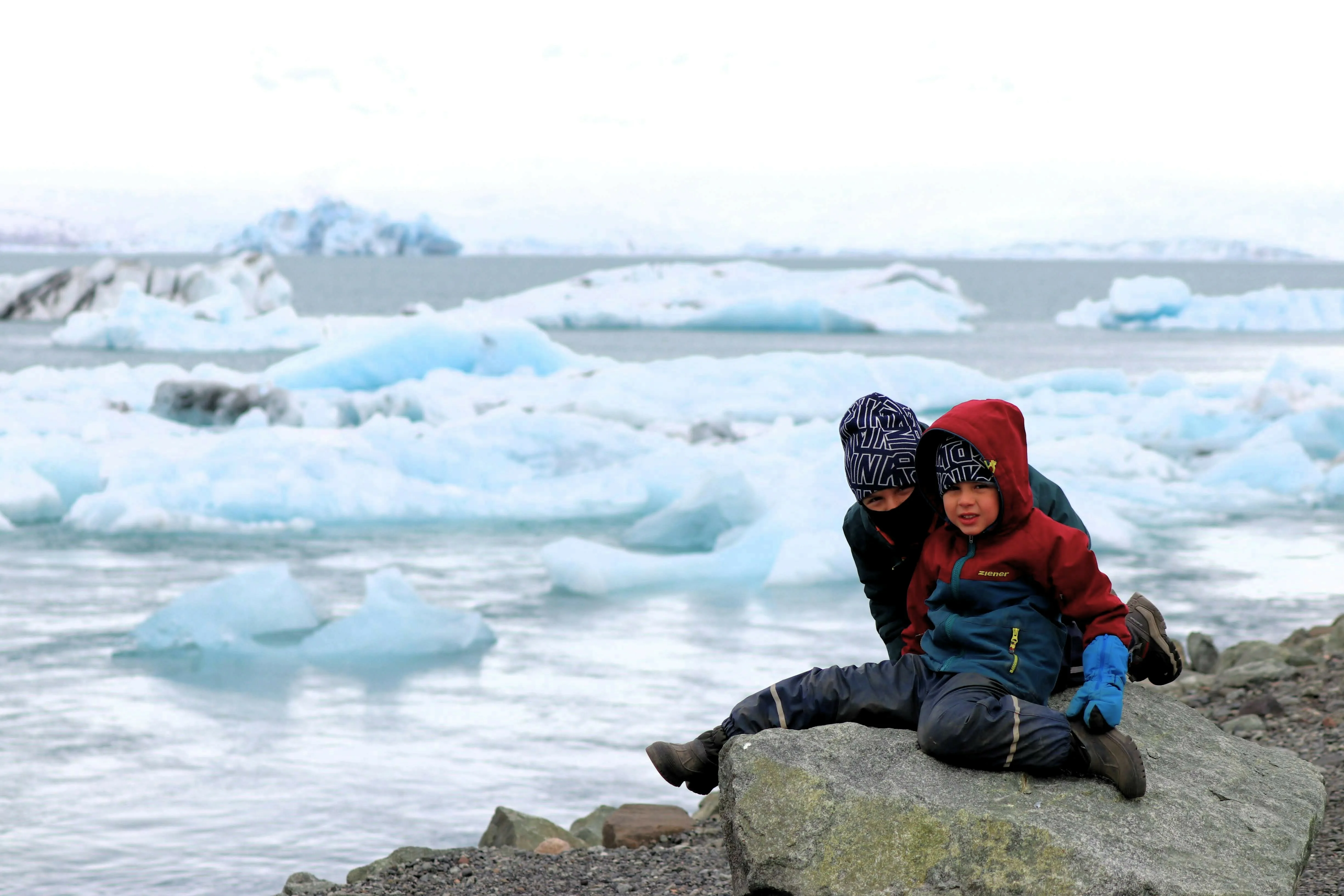 Zwei Jungen sitzen auf einem Felsen bei Jökulsárlón mit Eisbergen im Hintergrund