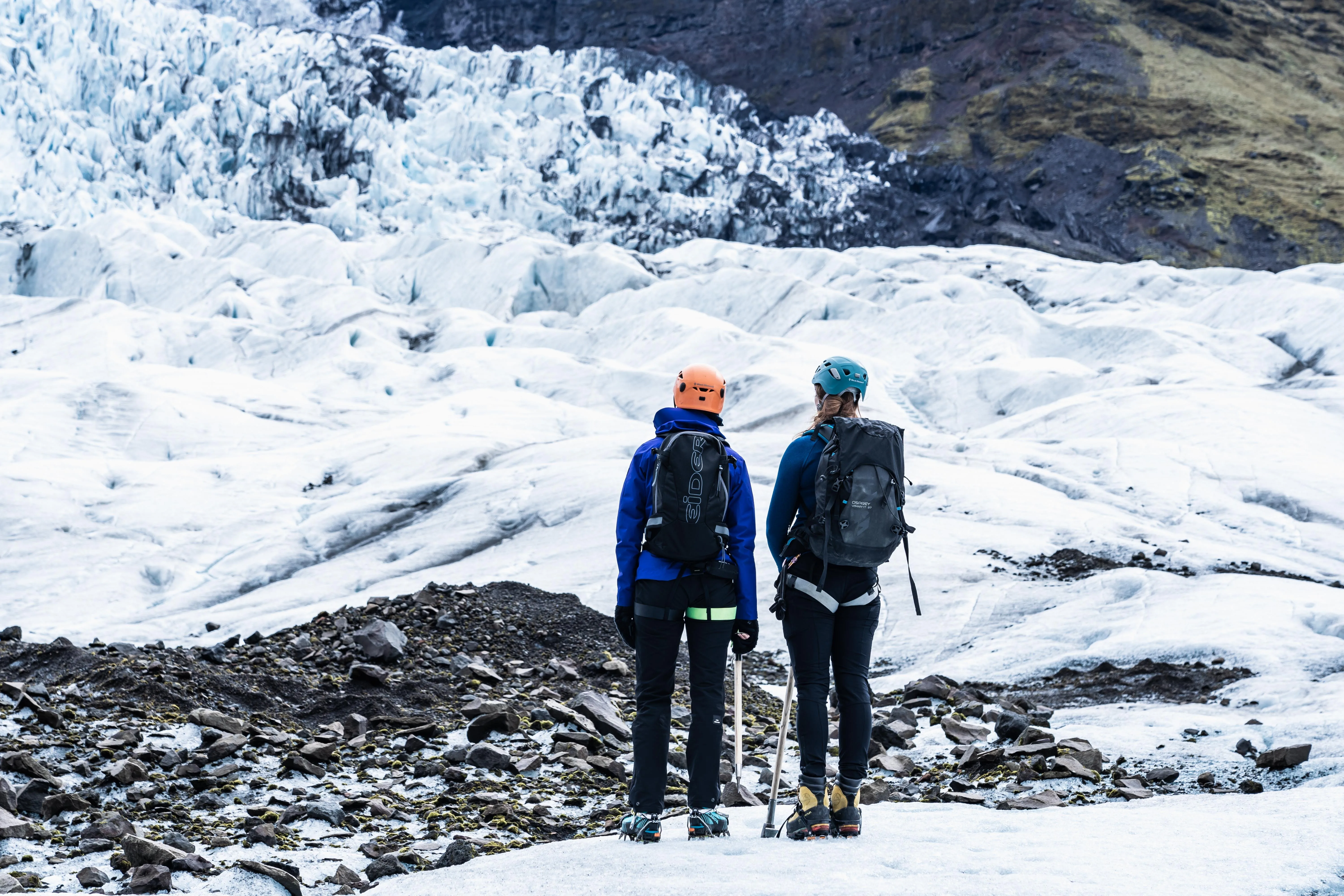 Zwei Personen stehen mit dem Rücken zur Kamera auf einem Gletscher und blicken nach oben.