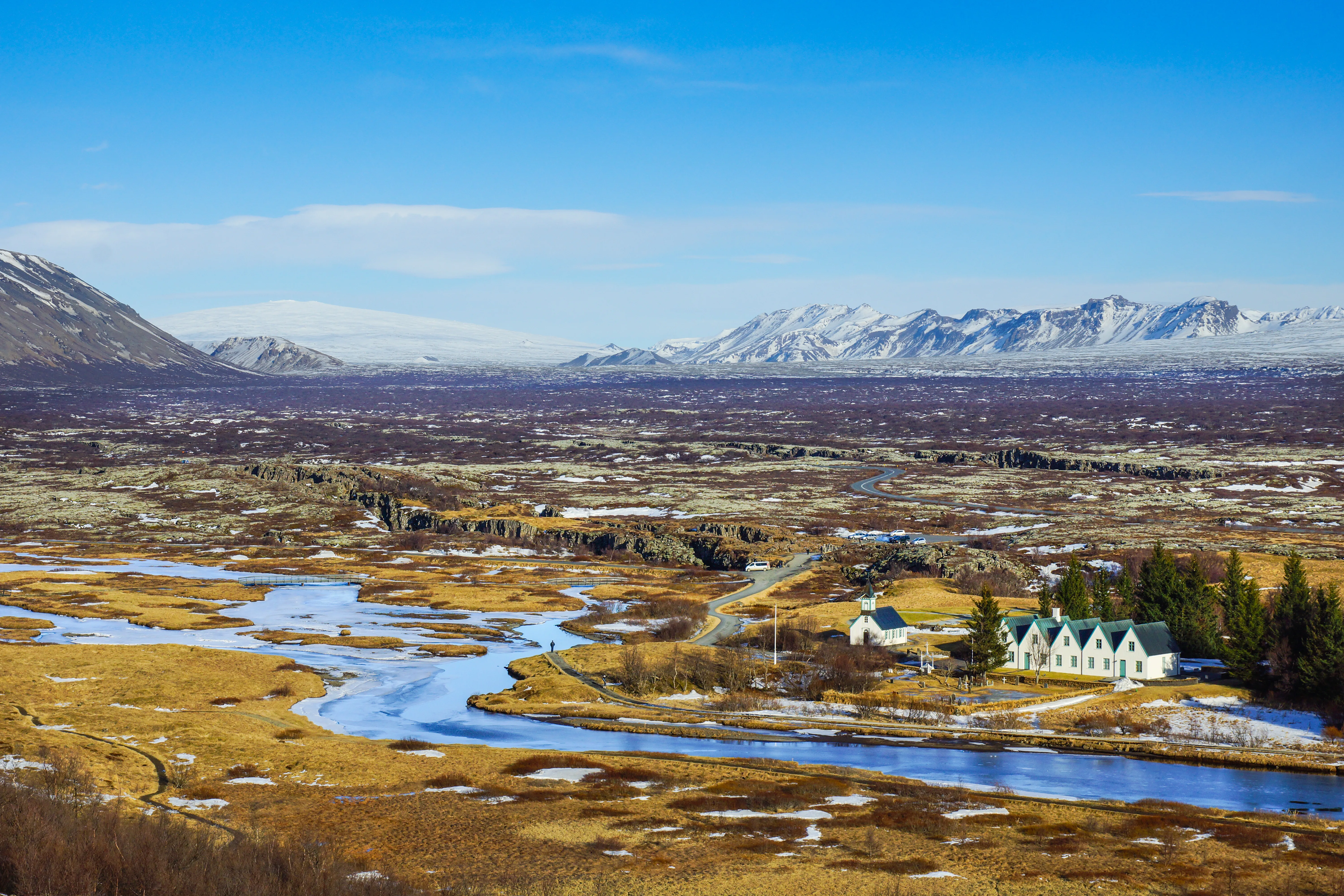 Blick auf den Þingvellir-Nationalpark in Südisland, wo ein Bach durch Moos und Felsen fließt und im Hintergrund Berge zu sehen sind