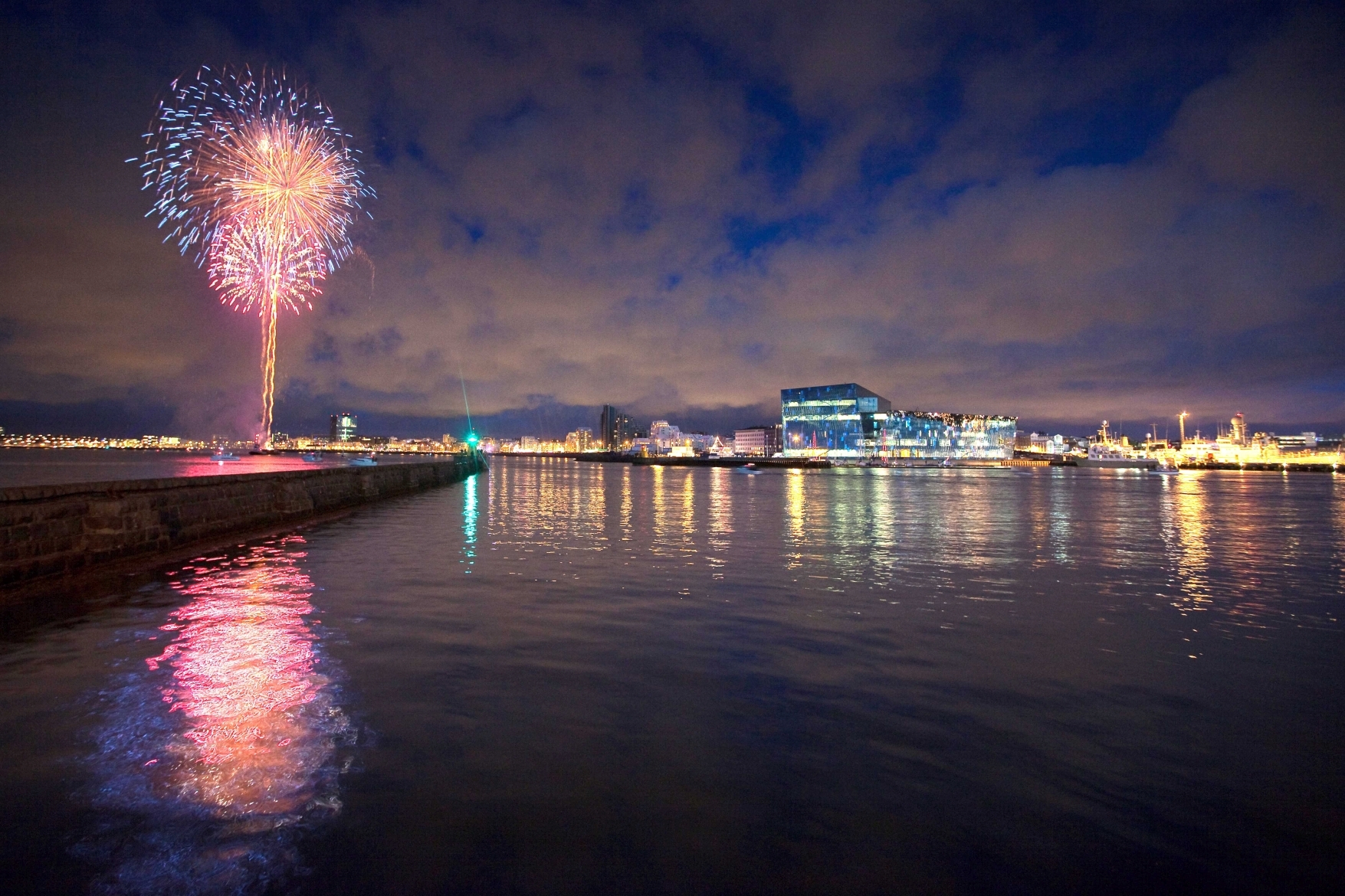 Silvester Reykjavik Harpa, Feuerwerk am Himmel, das sich im Wasser spiegelt. Lichter der Stadt und die Harpa am Horizont