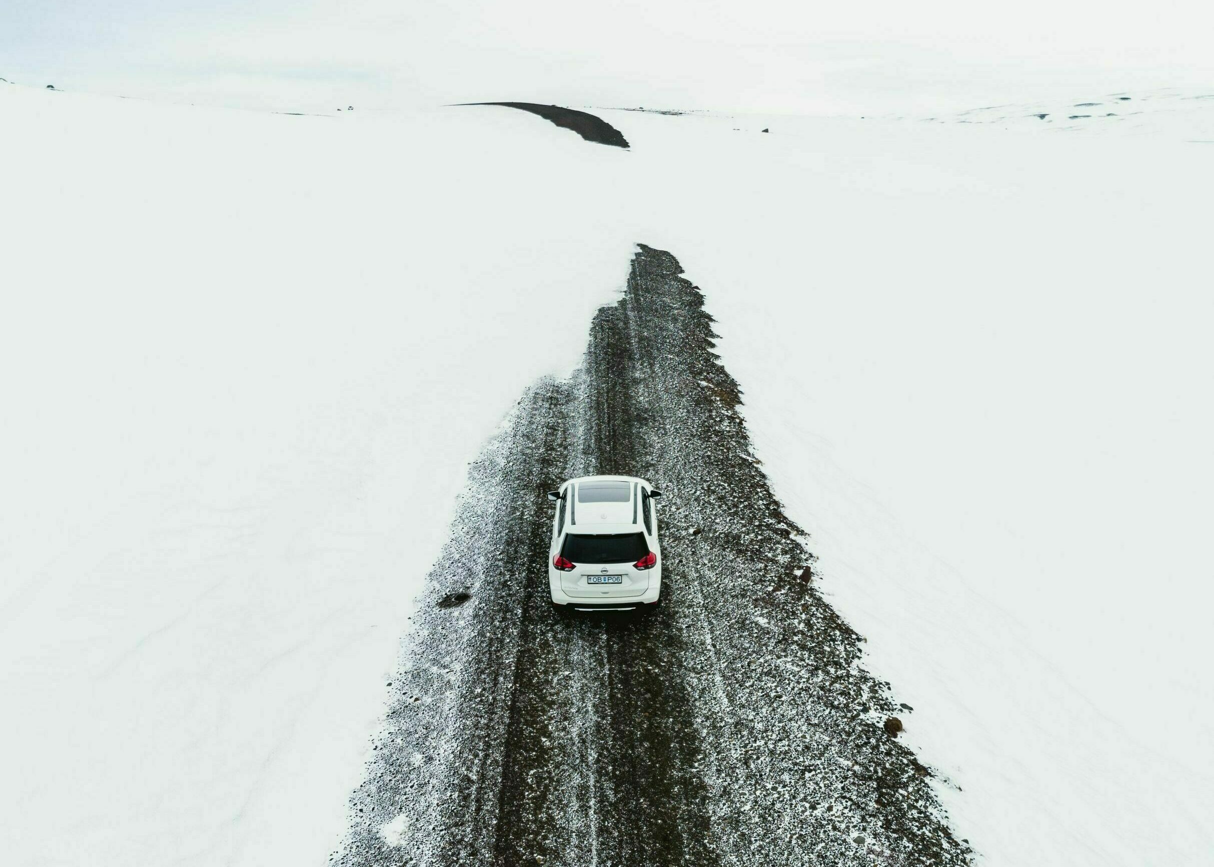 Straße mit Schnee in Westisland im Winter, weißes Auto fährt auf Straße, die Schneeverwehungen hat, rund um die Straße ist alles weiß