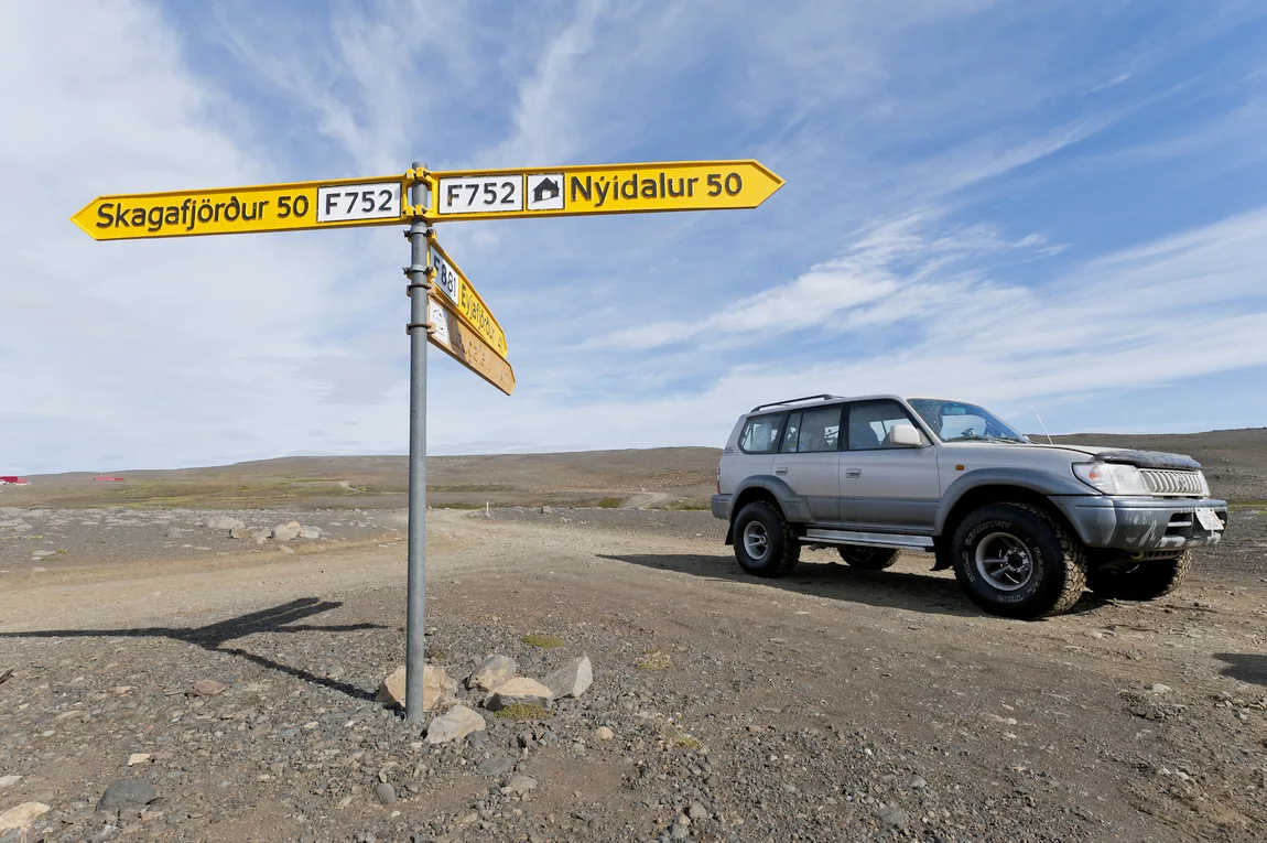 Grauer Jeep steht in Islands Hochland neben einem Wegweiser