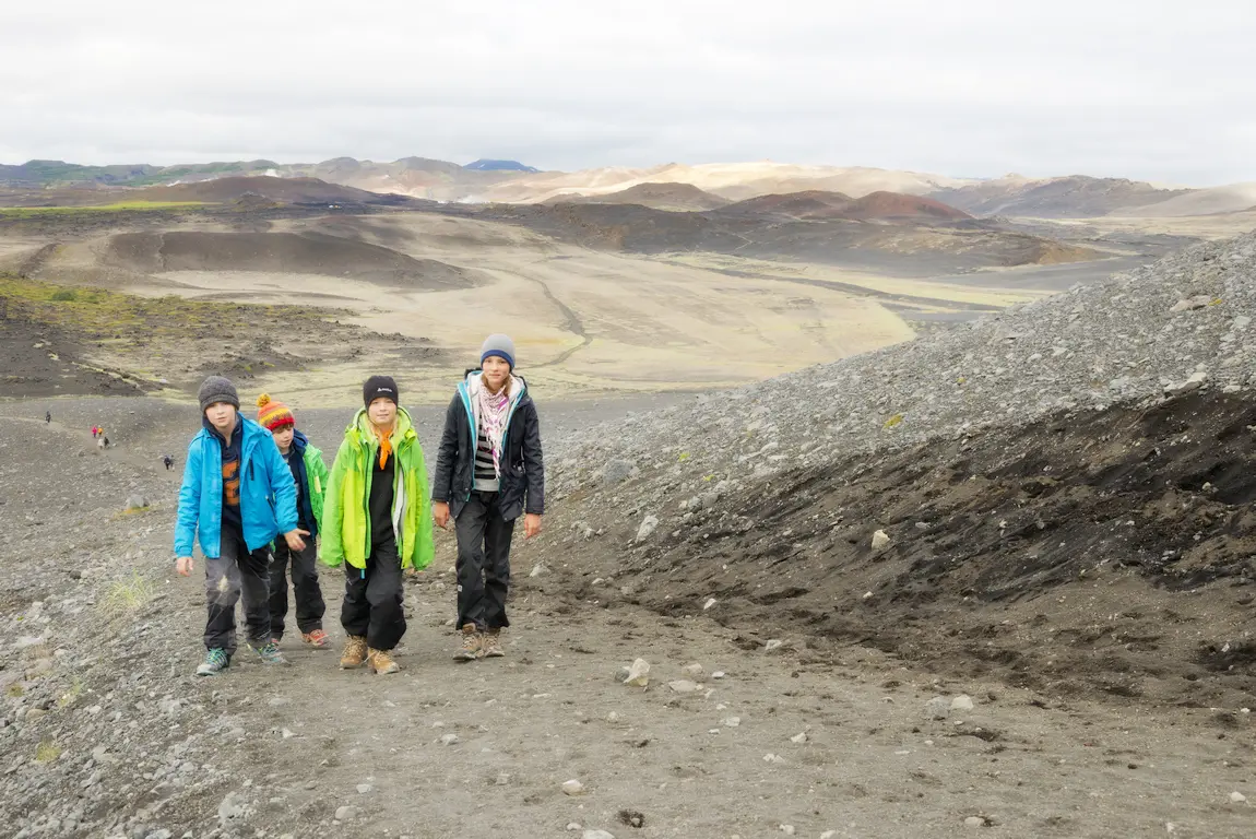 Vier Wanderer in bunter Kleidung gehen durch eine karge, vulkanische Landschaft in Island