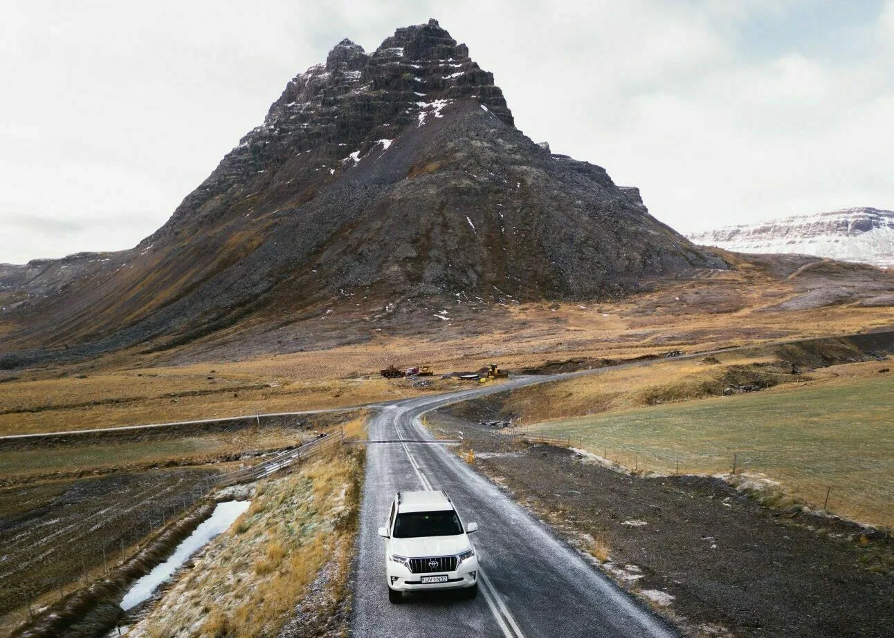 Ein Auto fährt auf einer Straße vor dramatischer Bergkulisse im Hintergrund