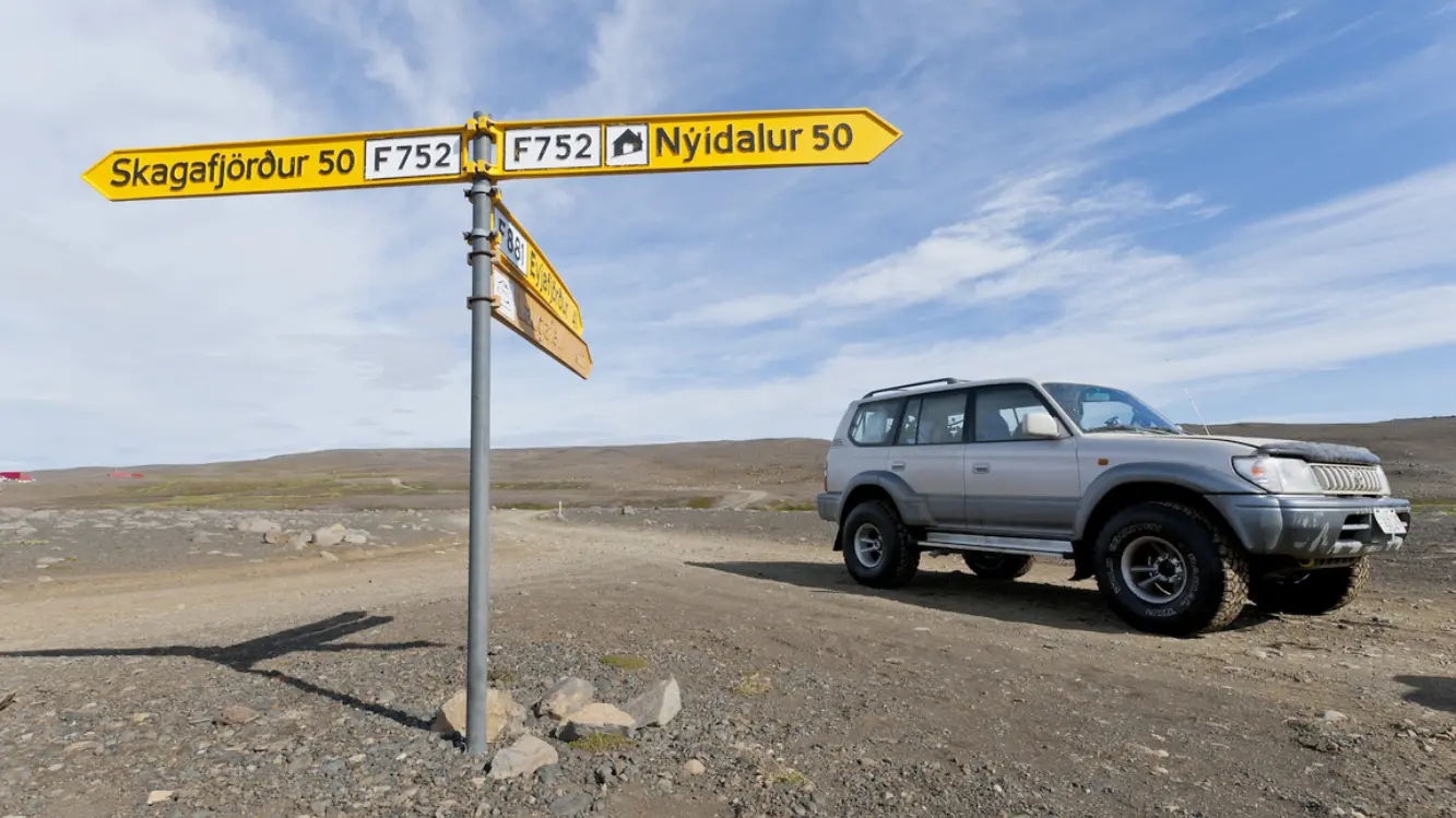 Islands Hochland - Kjölur Route Grauer Jeep steht in Islands Hochland neben einem Wegweiser
