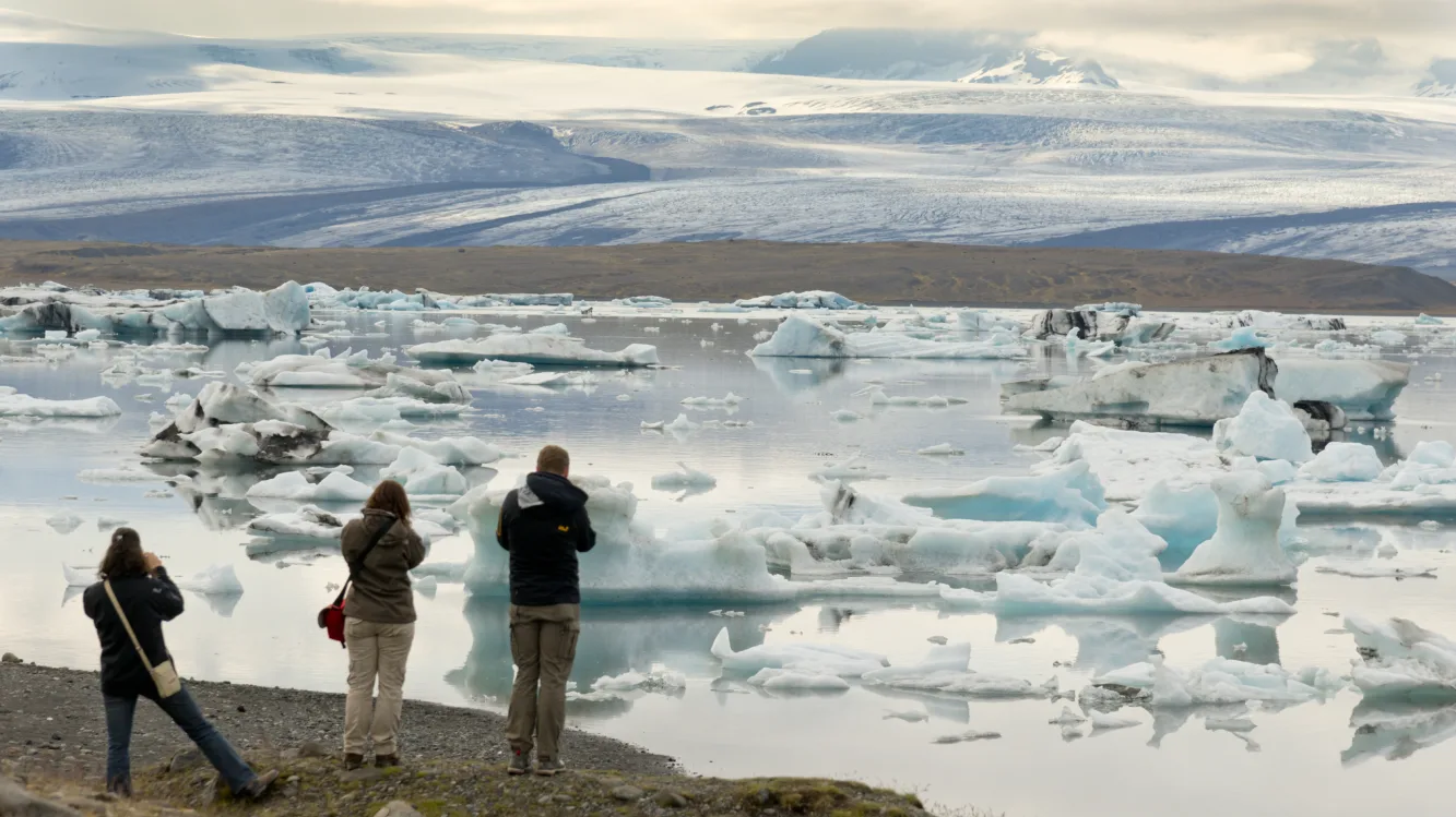 Südisland Gletscherlagune Jökulsarlon
Drei Personen betrachten die Gletscherlagune Jökulsarlon und schießen Fotos. Die Lagune ist voll mit Eisbrocken. Im Hintergrund sieht man den Gletscher Vatnajökull.