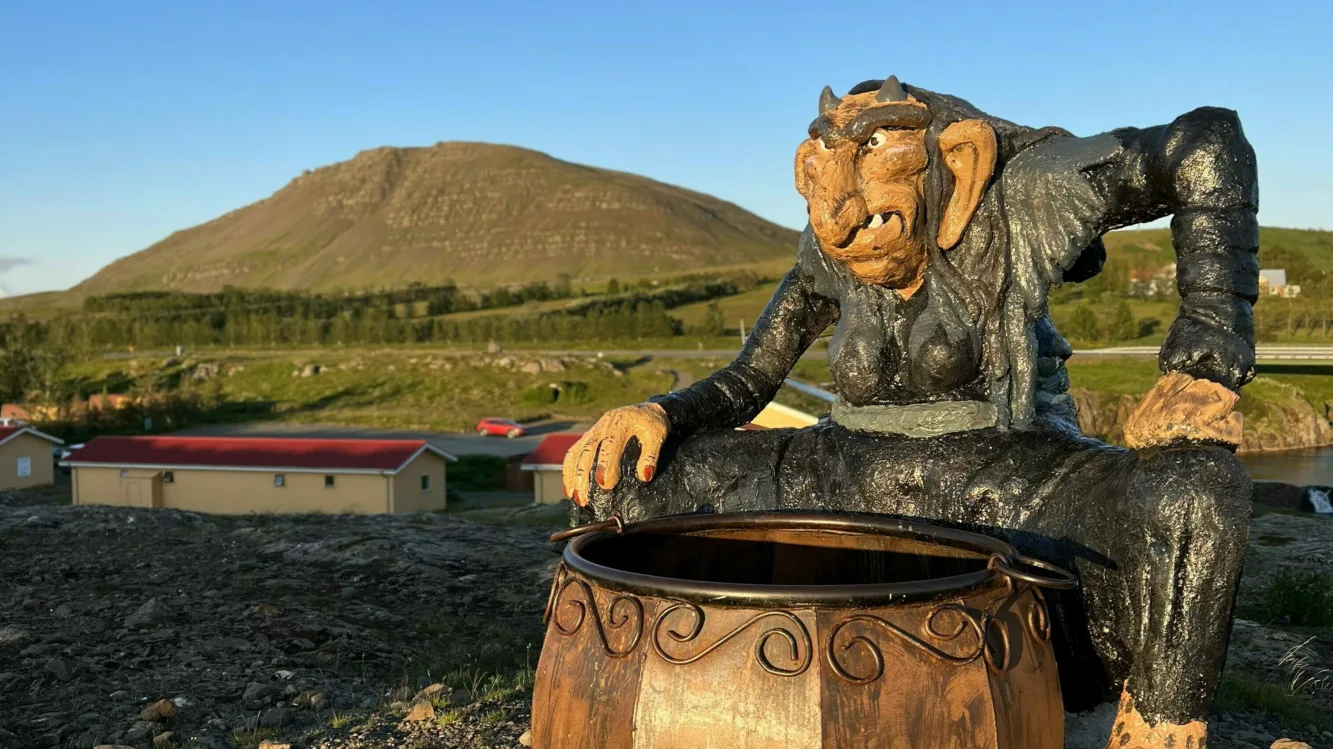 Ein Troll im Trollgarten in Island, der einen großen Kochtopf vor sich stehen hat