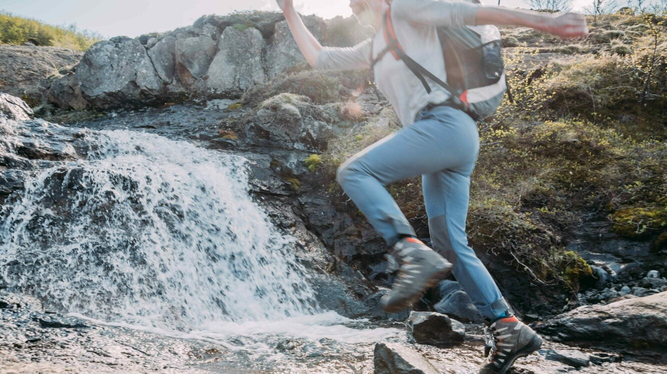 Mitarbeiterin von Katla Travel springt über einen Bach in Island
