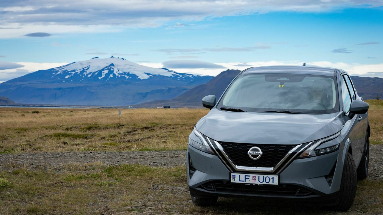 Island Mietwagen ein grauen Nissan SUV steht in Islands Ebene. Im Hintergrund ein mit Schnee bedeckter Berg