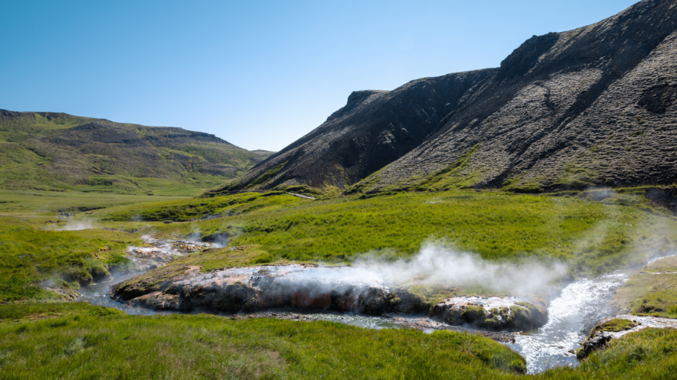 Reykjadalur; 
dampfender Bach schlängelt sich in einem grünen Tal entlang