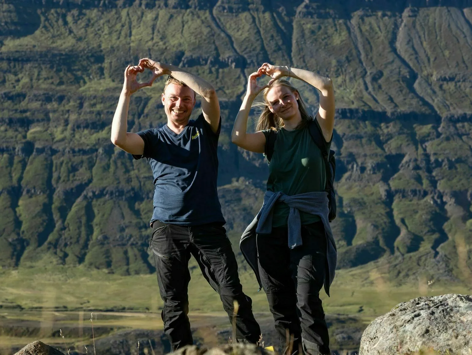 2 Wanderer halten ihre Hände hoch zum Herz geformt in der isländischen Landschaft