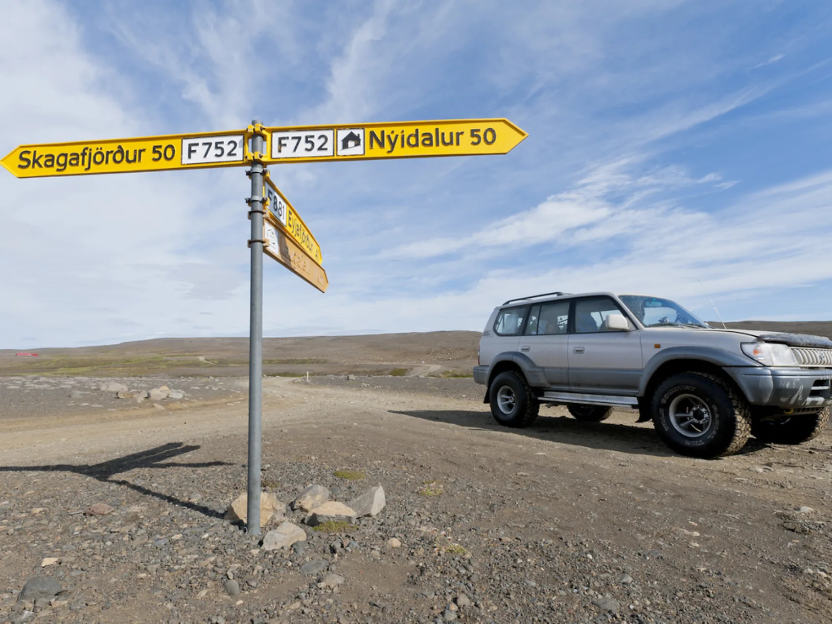 Grauer Jeep steht in Islands Hochland neben einem Wegweiser