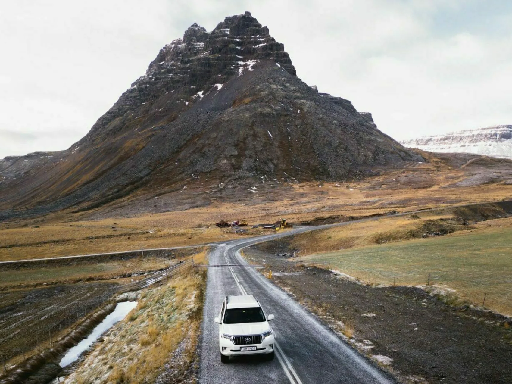 Ein Auto fährt auf einer Straße vor dramatischer Bergkulisse im Hintergrund