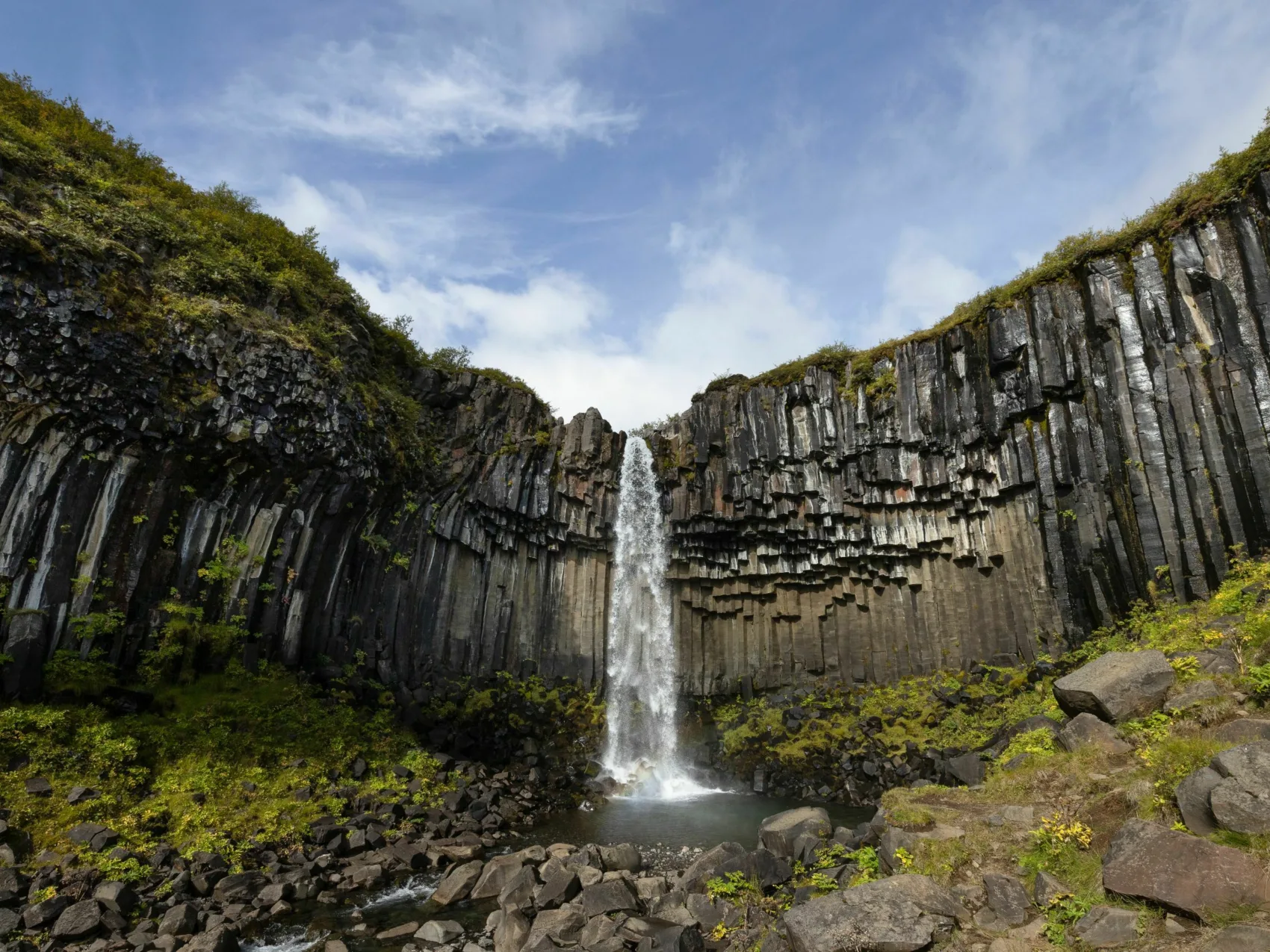 Island Wasserfall Svartifoss, Foto: Timo Klingebiel
Zwischen Basaltsäulen stürzt das Wasserfall des Svartifoss in die Tiefe
Der Himmel ist blau mit leichten Wolken.