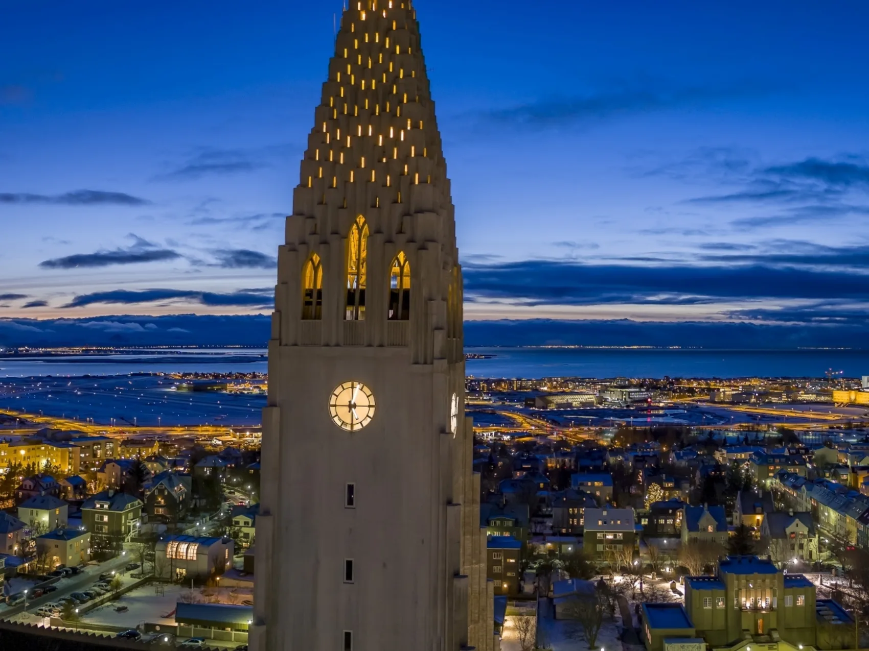 Reykjavik Hallgrímskirkja bei Dunkelheit im Vordergrund mit Lichtern der Stadt im Hinergrund, leichte Dämmerung im Hintergrund