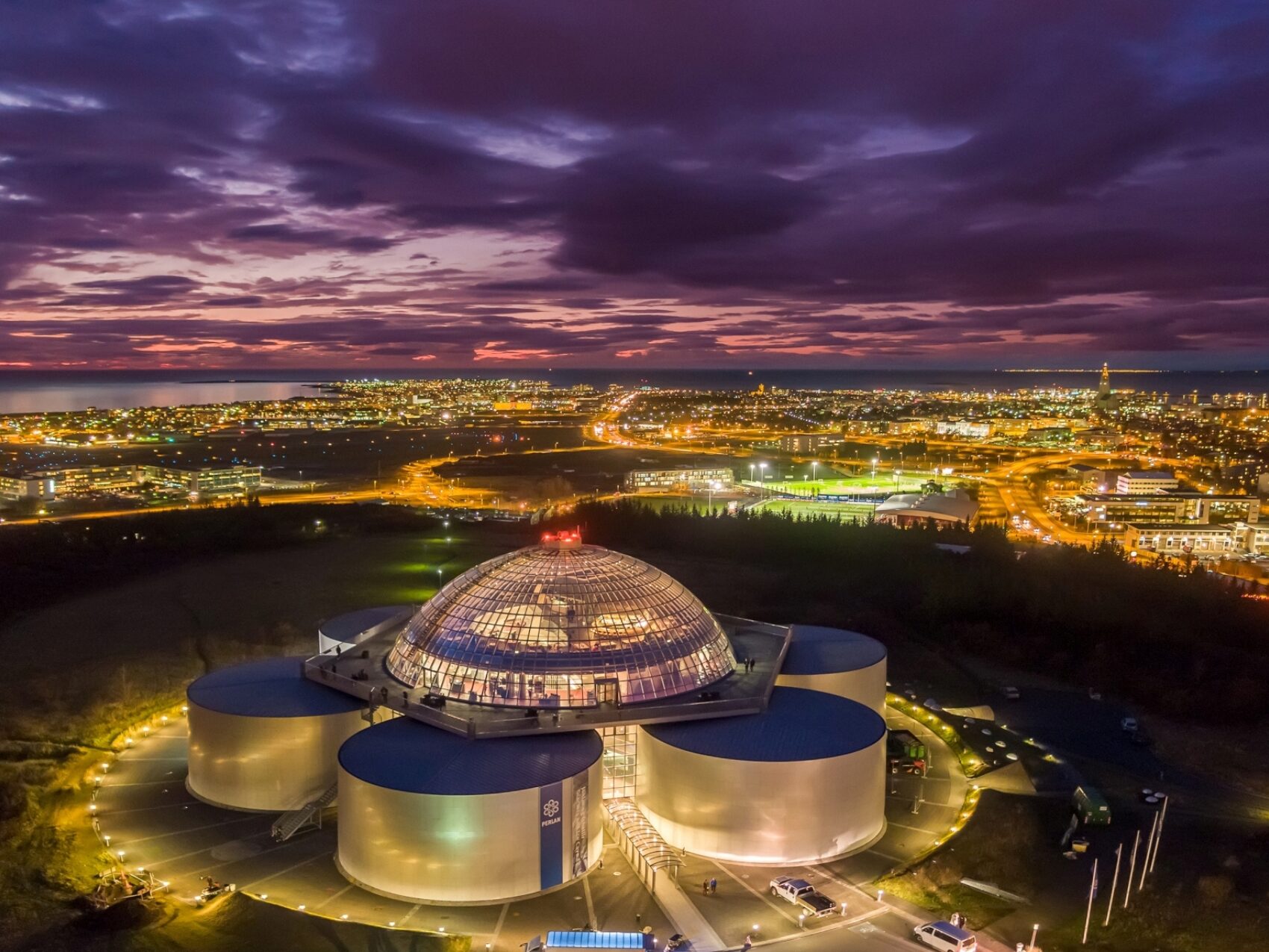 Perlan Reykjavík bei Nacht, von oben fotografiert - die Stadt im Hintergrund leuchtet, lila Himmel