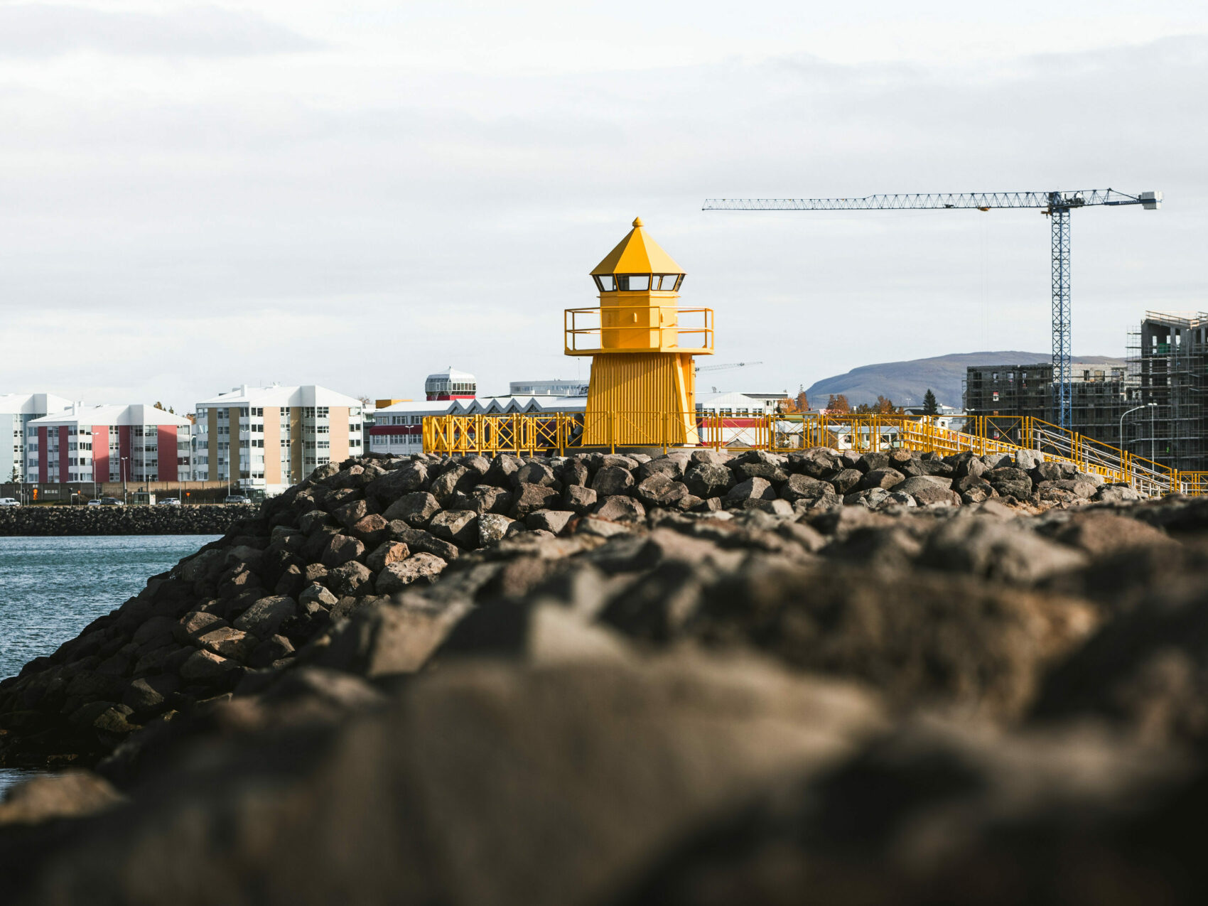 Reykjavík Höfði Leuchtturm, in Gelb auf Steinen - im Hintergrund hohe Gebäude und zwei Krähne