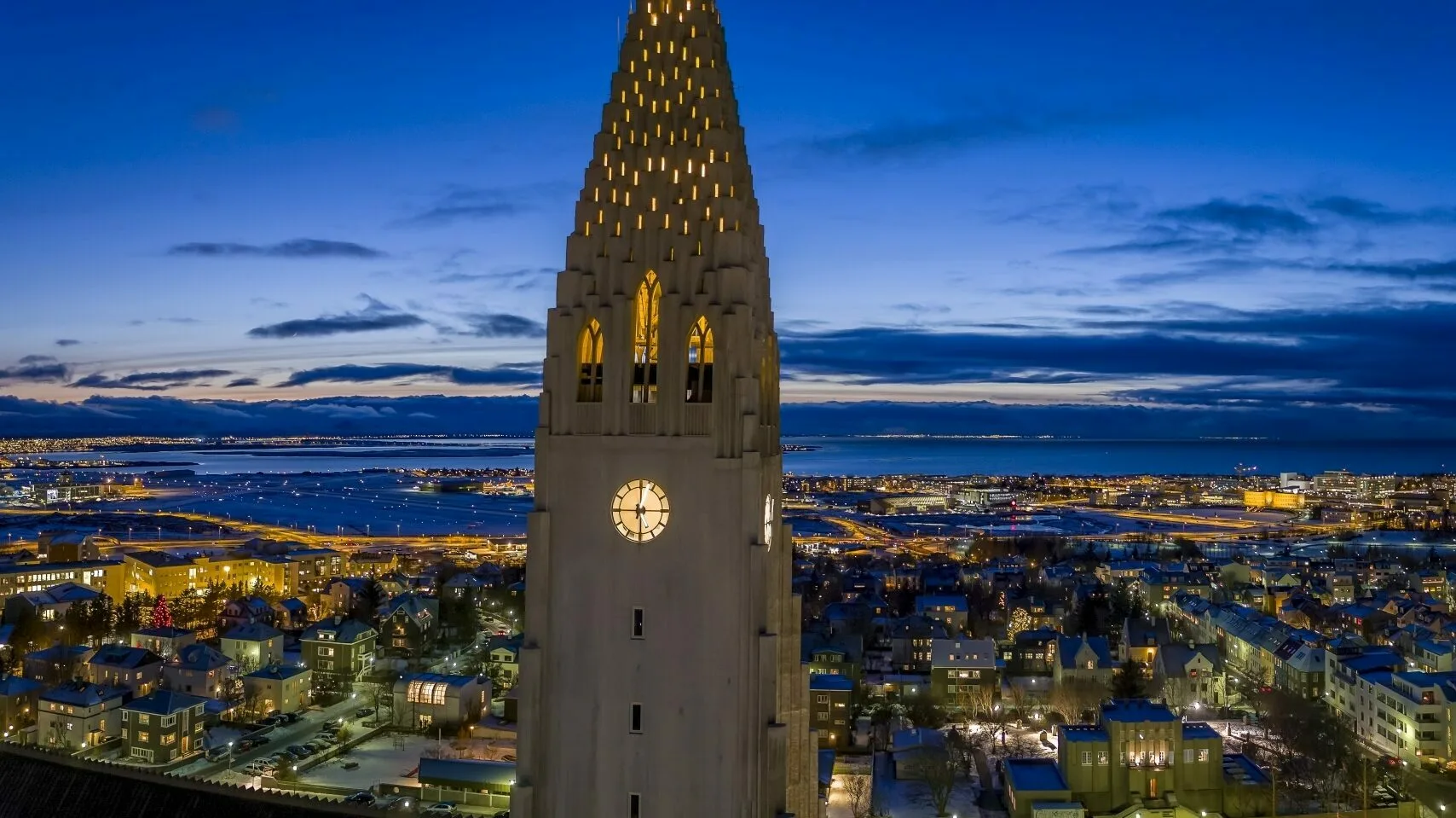 Reykjavik Hallgrímskirkja bei Dunkelheit im Vordergrund mit Lichtern der Stadt im Hinergrund, leichte Dämmerung im Hintergrund