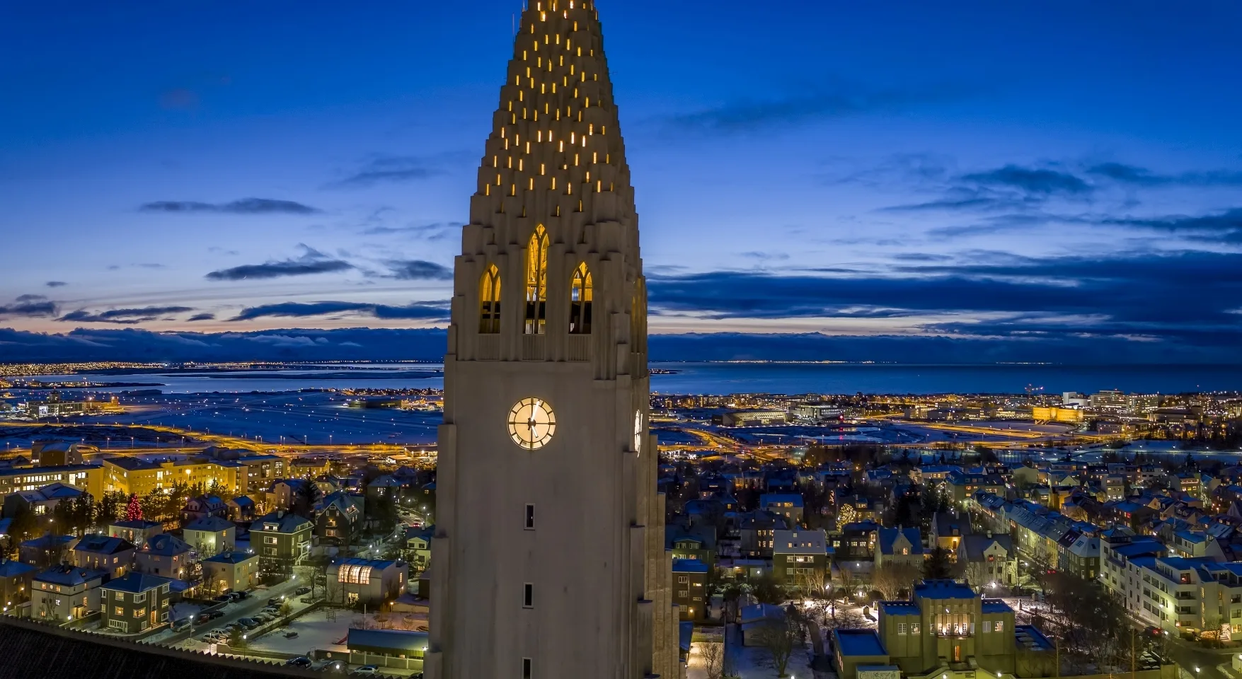 Reykjavik Hallgrímskirkja bei Dunkelheit im Vordergrund mit Lichtern der Stadt im Hinergrund, leichte Dämmerung im Hintergrund