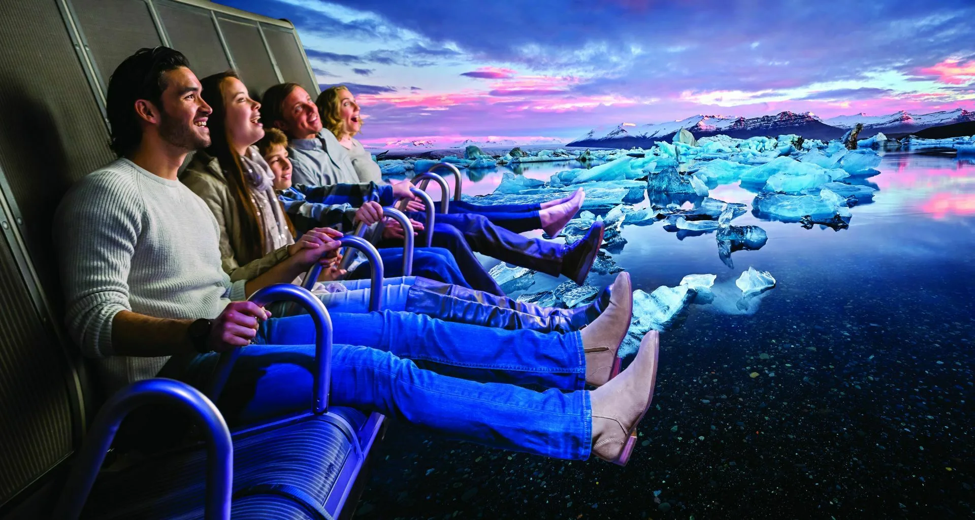 Fünf Touristen sitzen lachend in der Fly Over Iceland Attraktion in Island, während sie über den Diamond Beach fliegen