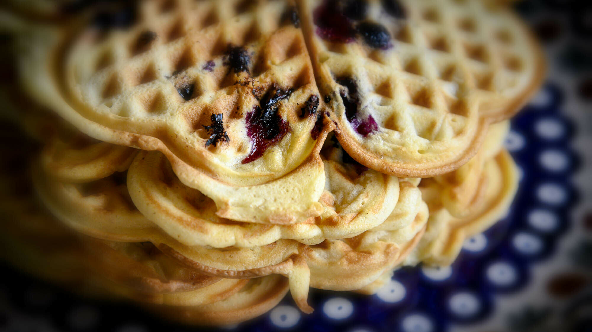 Waffeln mit Blaubeermarmelade in Herzform gestapelt auf einem blauen Teller mit weißen Punkten