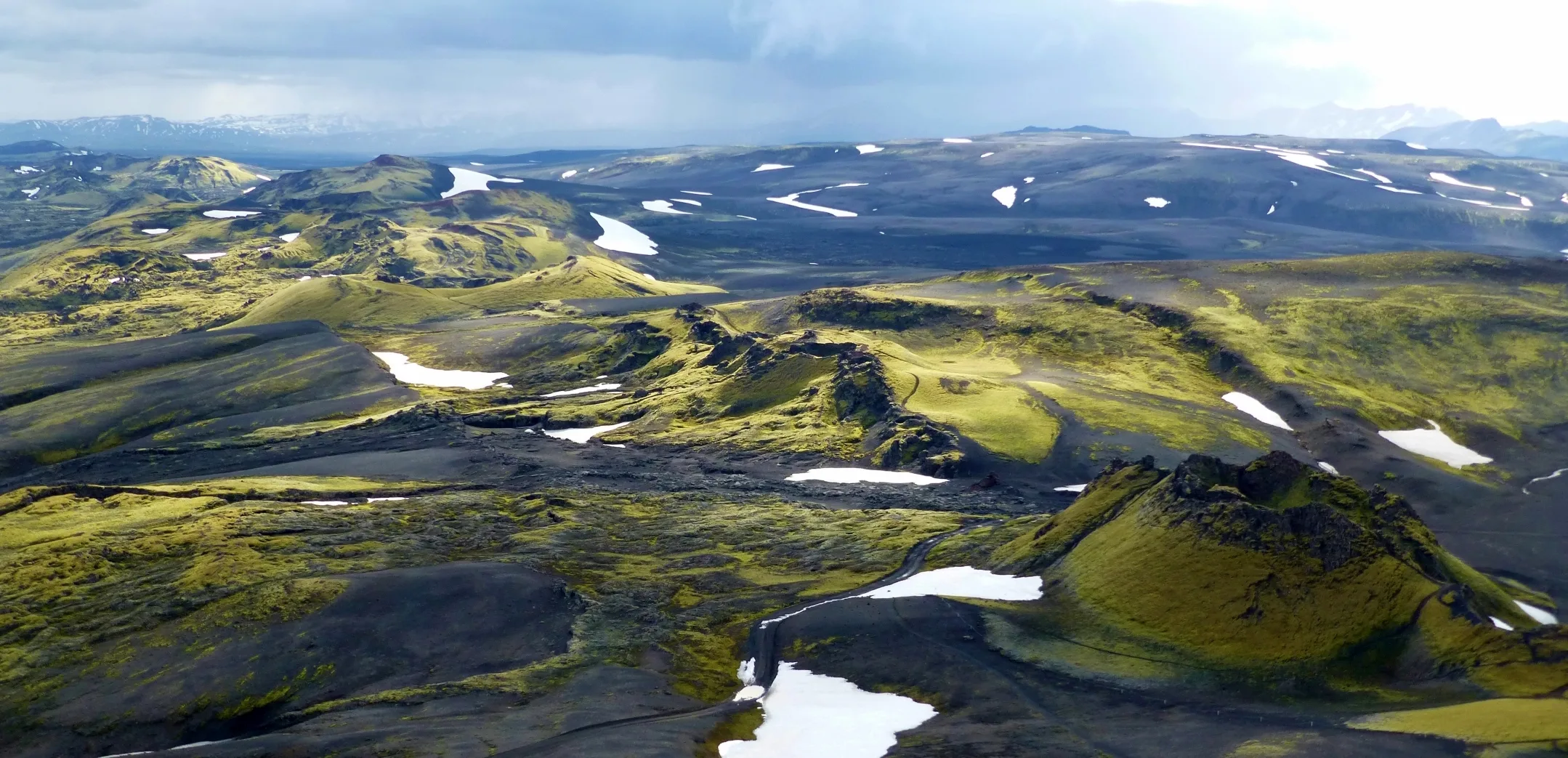 Luftaufnahme einer hügeligen grünbraunen isländischen Landschaft, die teilweise leicht mit Schnee bedeckt ist