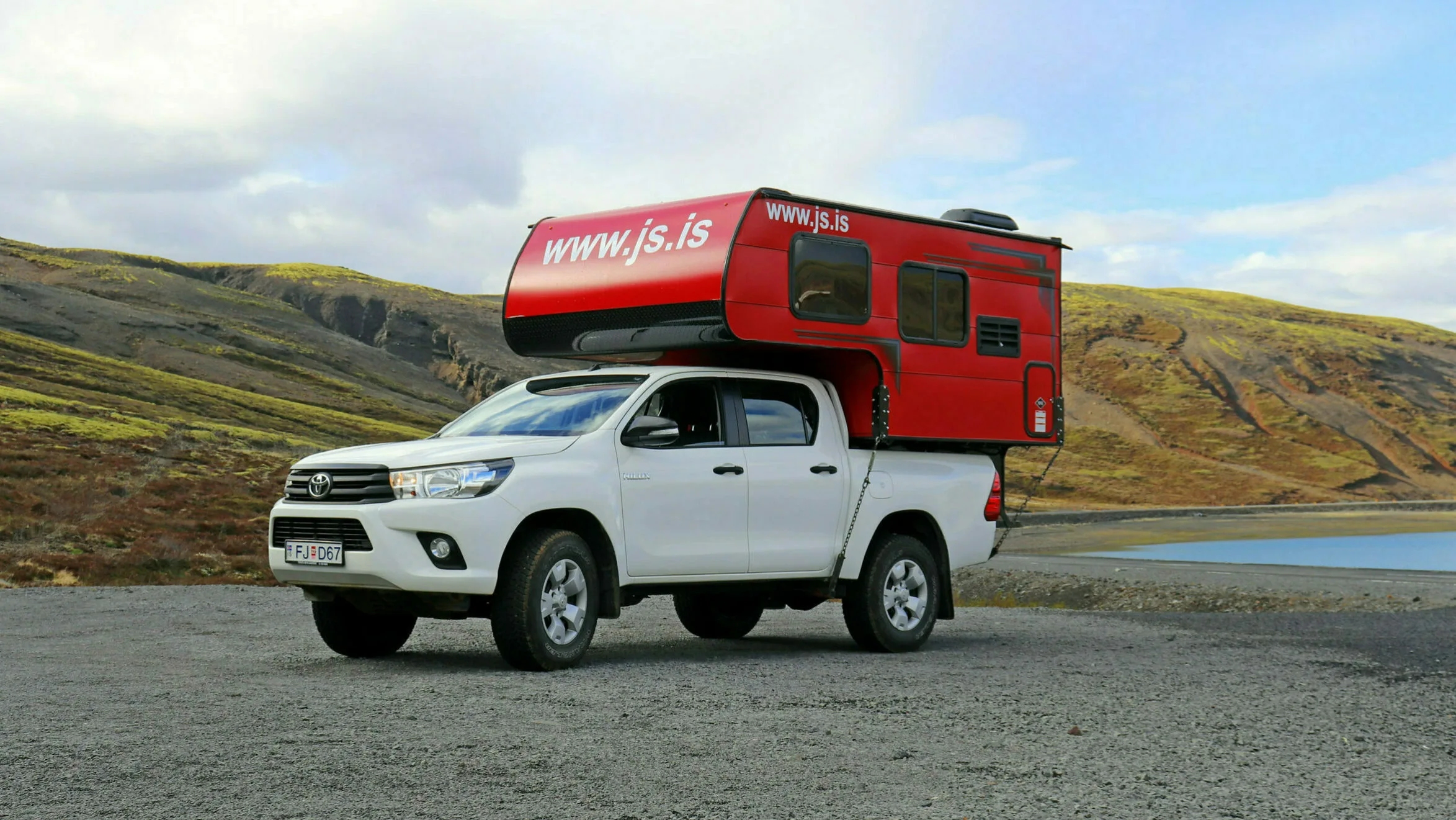 Ein Truckcamper steht neben einem See in bergiger isländischer Landschaft