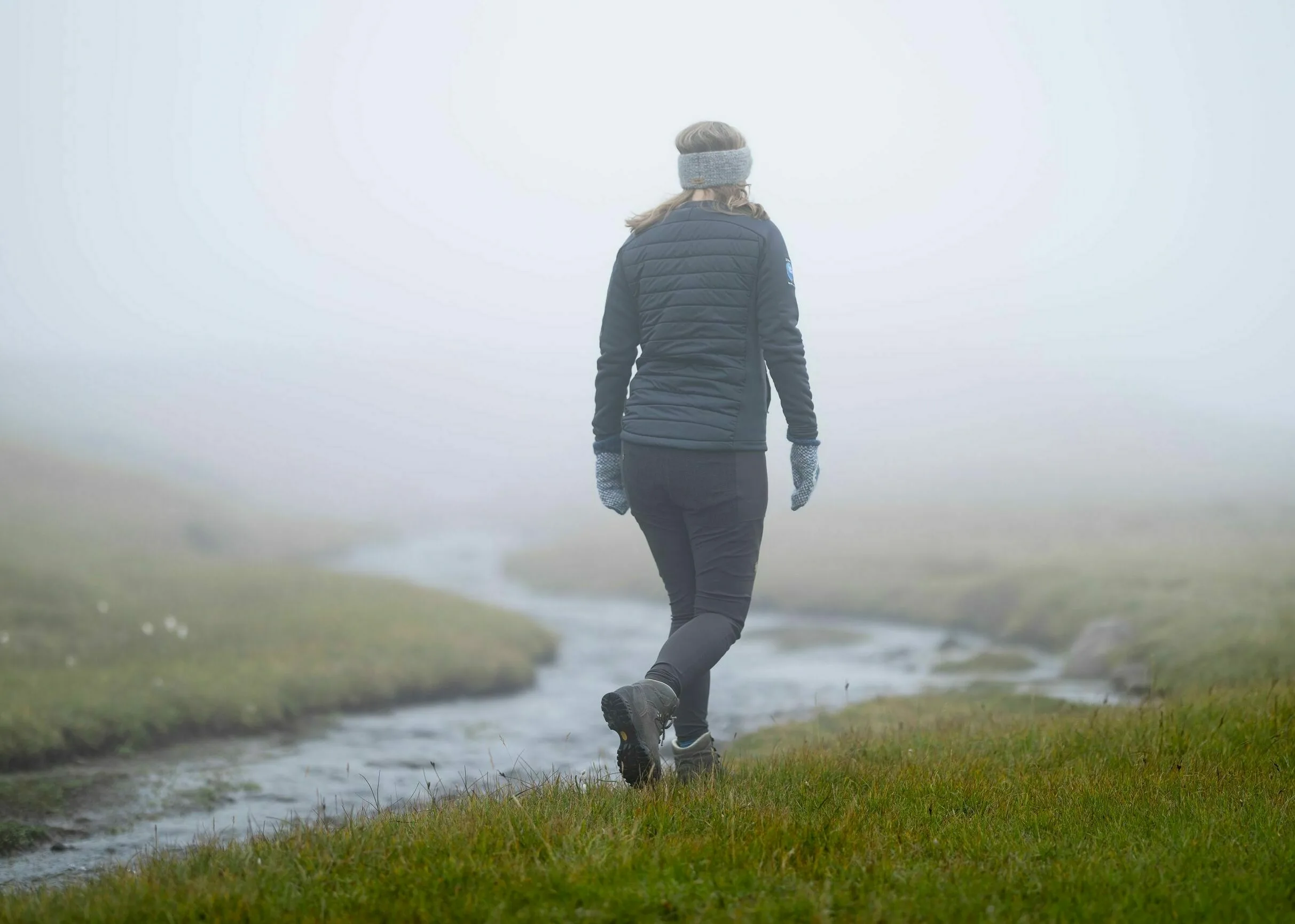 Island - Wanderin im Nebel läuft an einem Fluss entlang auf grünem Gras