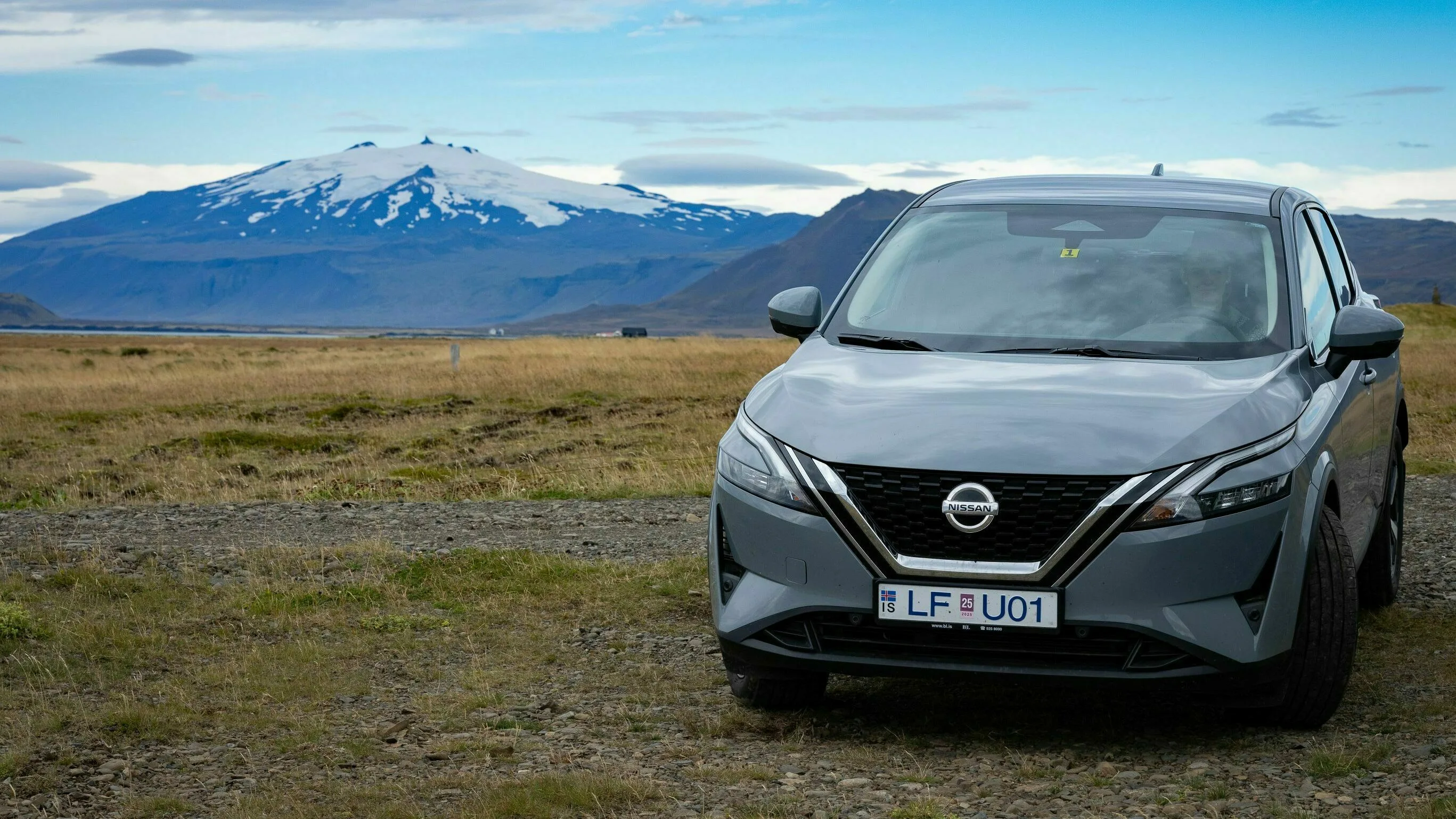 Ein grauer Mietwagen steht in isländischer Landschaft mit verschneiten Bergen im Hintergrund