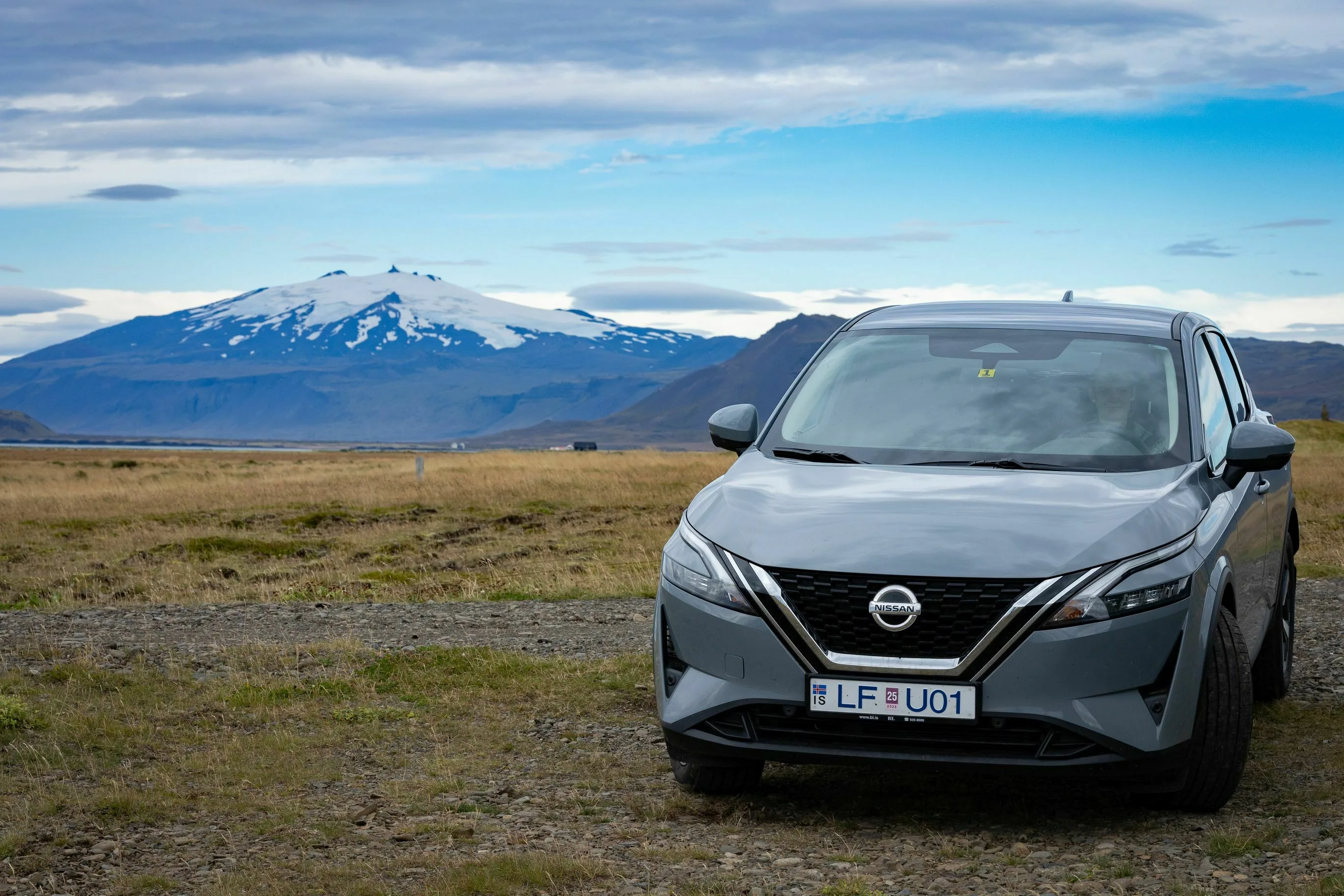 Island Mietwagen ein grauen Nissan SUV steht in Islands Ebene. Im Hintergrund ein mit Schnee bedeckter Berg