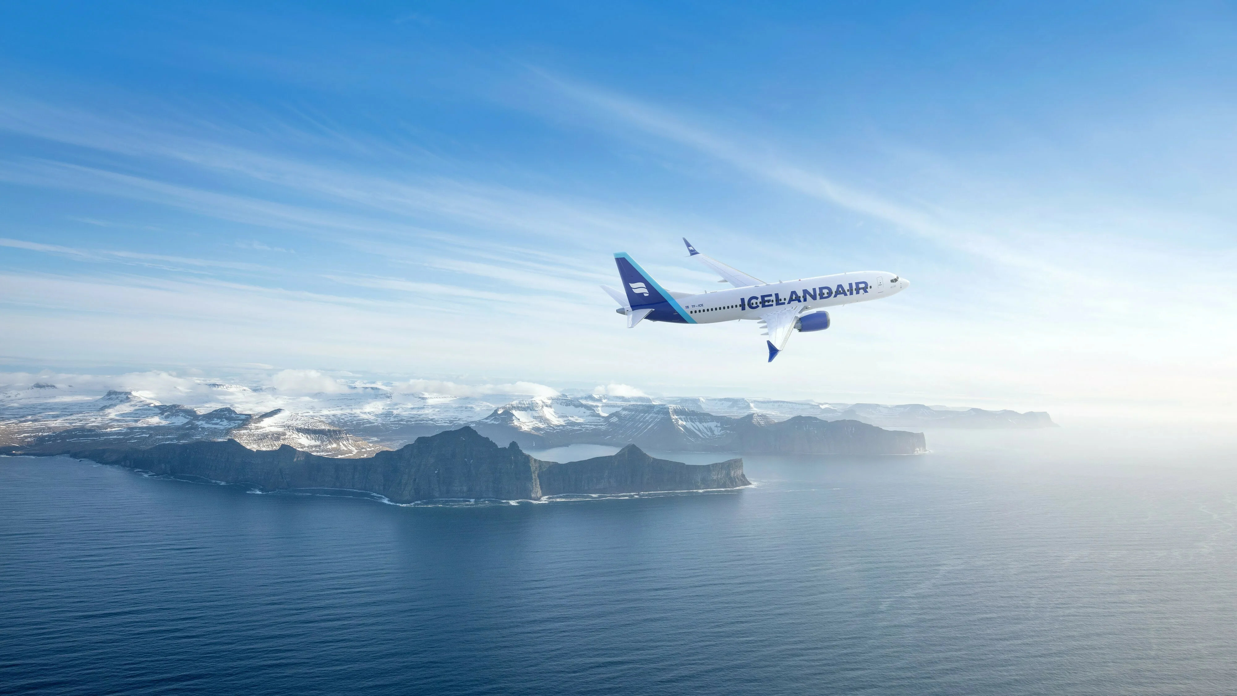 Luftaufnahme eines Flugzeugs von Icelandair, welches über dem Meer neben den verschneiten Bergen an der Küste Islands fliegt