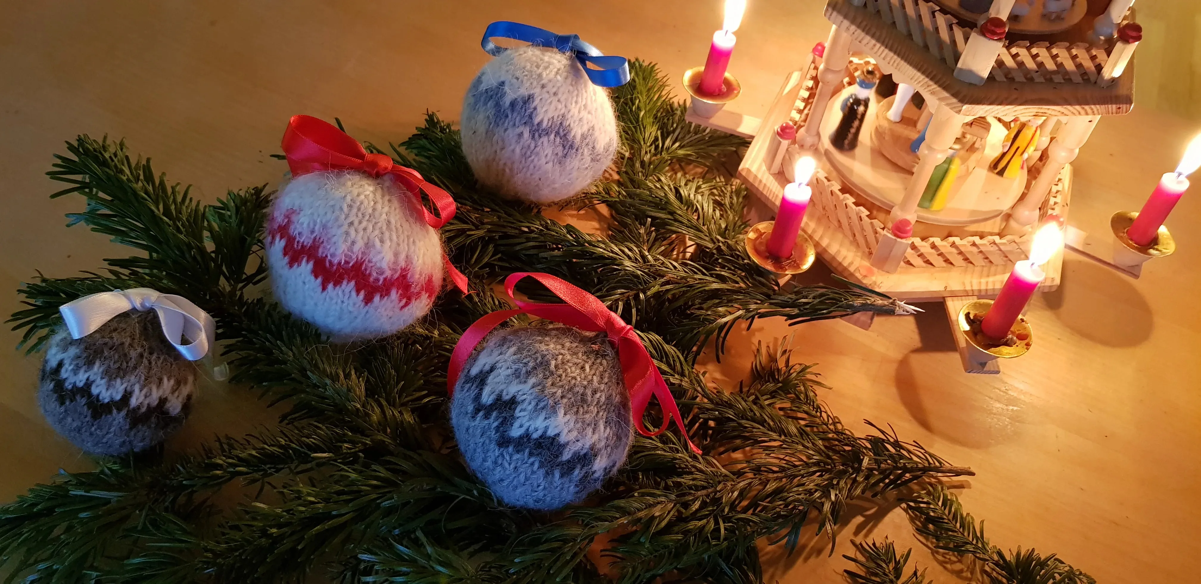 Ein Tannenzweig mit mehreren Christbaumkugeln aus Wolle mit Mustern