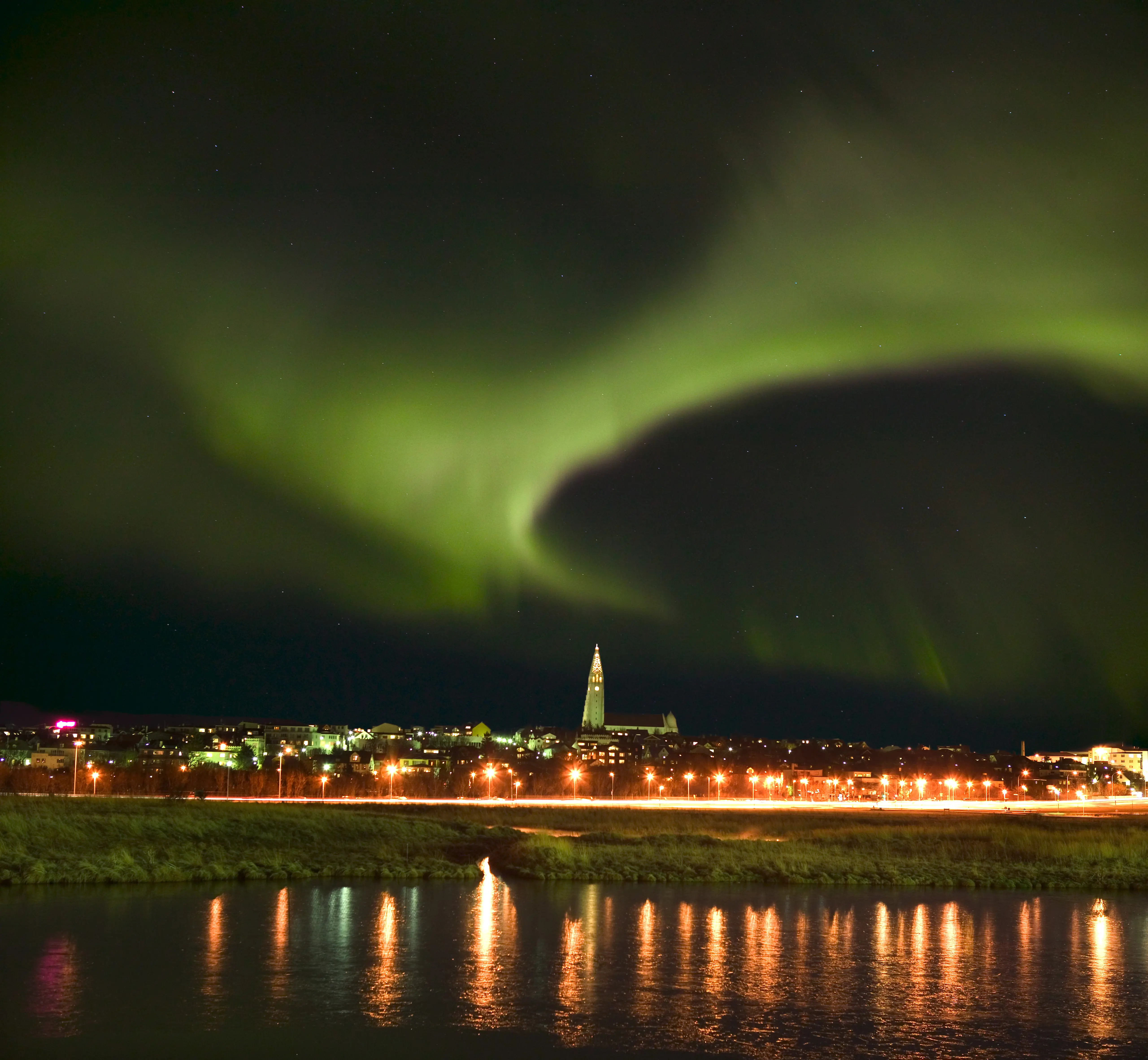 Aufnahme vom Meer aus von Reykjavik mit der Hallgrimskirkja Kirche in der Mitte und imposanten Nordlichtern im Himmel