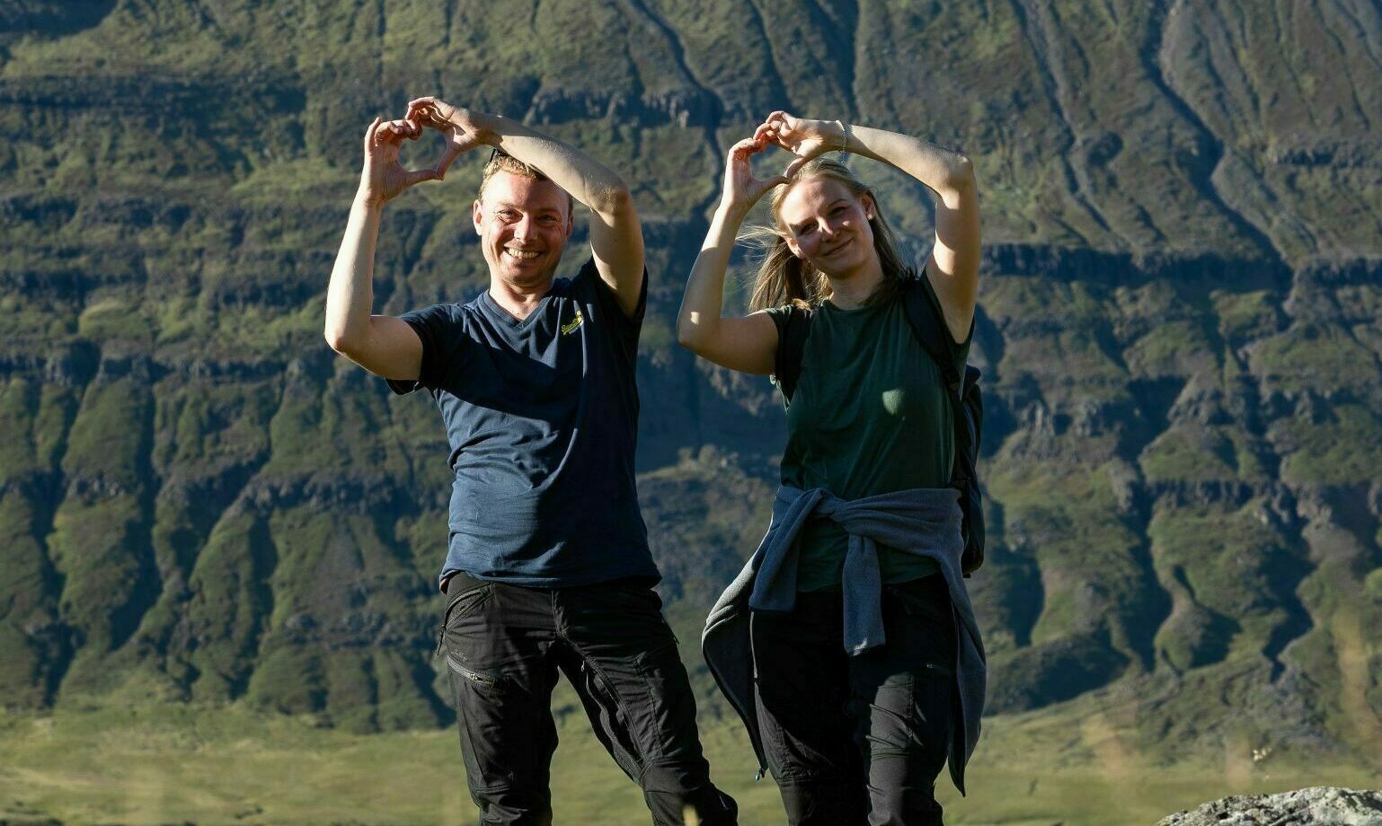 2 Wanderer halten ihre Hände hoch zum Herz geformt in der isländischen Landschaft