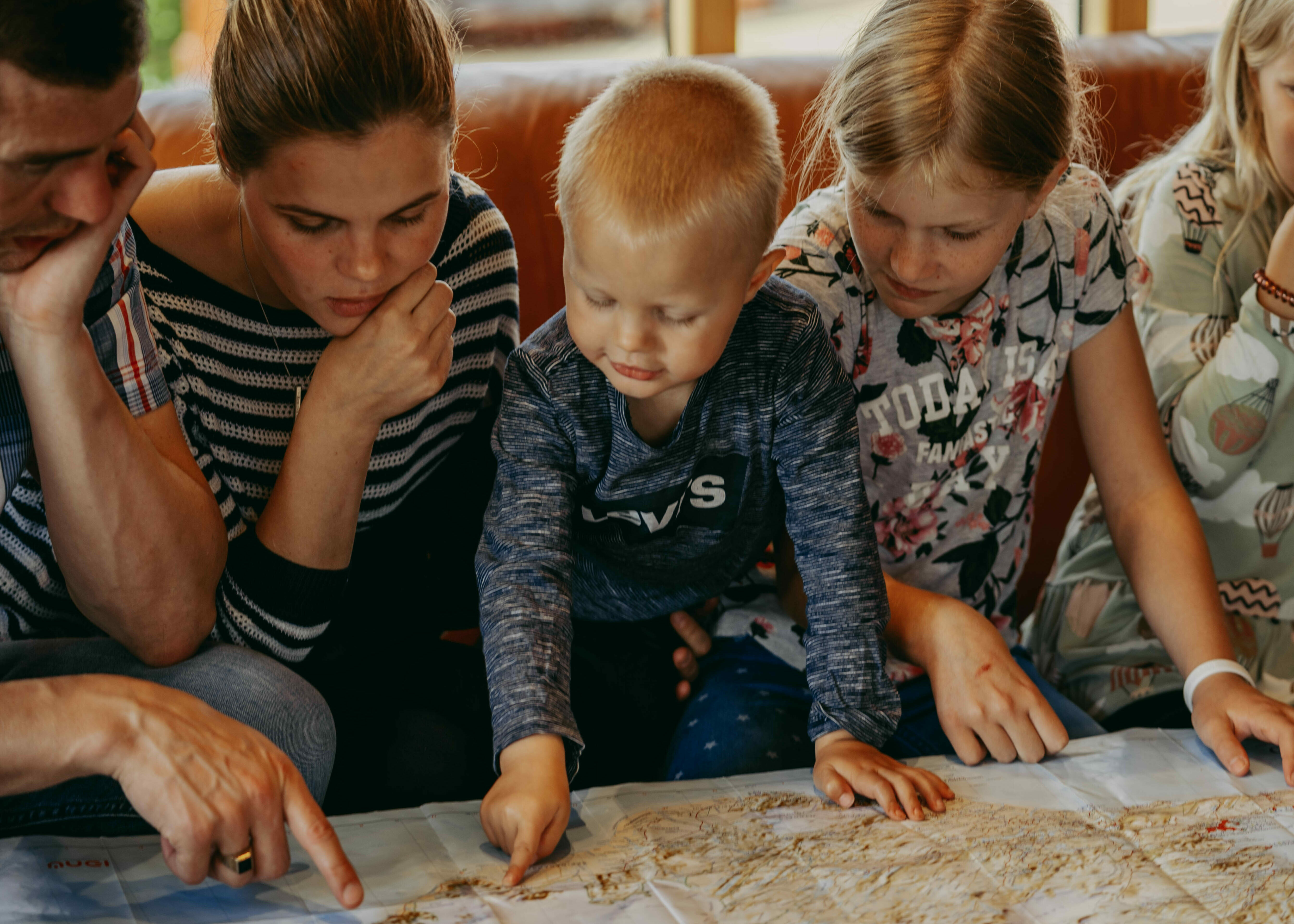 Island Reiseplanung mit der Familie, Eltern sitzen mit Kindern um eine Karte und deuten mit den Fingern auf bestimmte Stellen