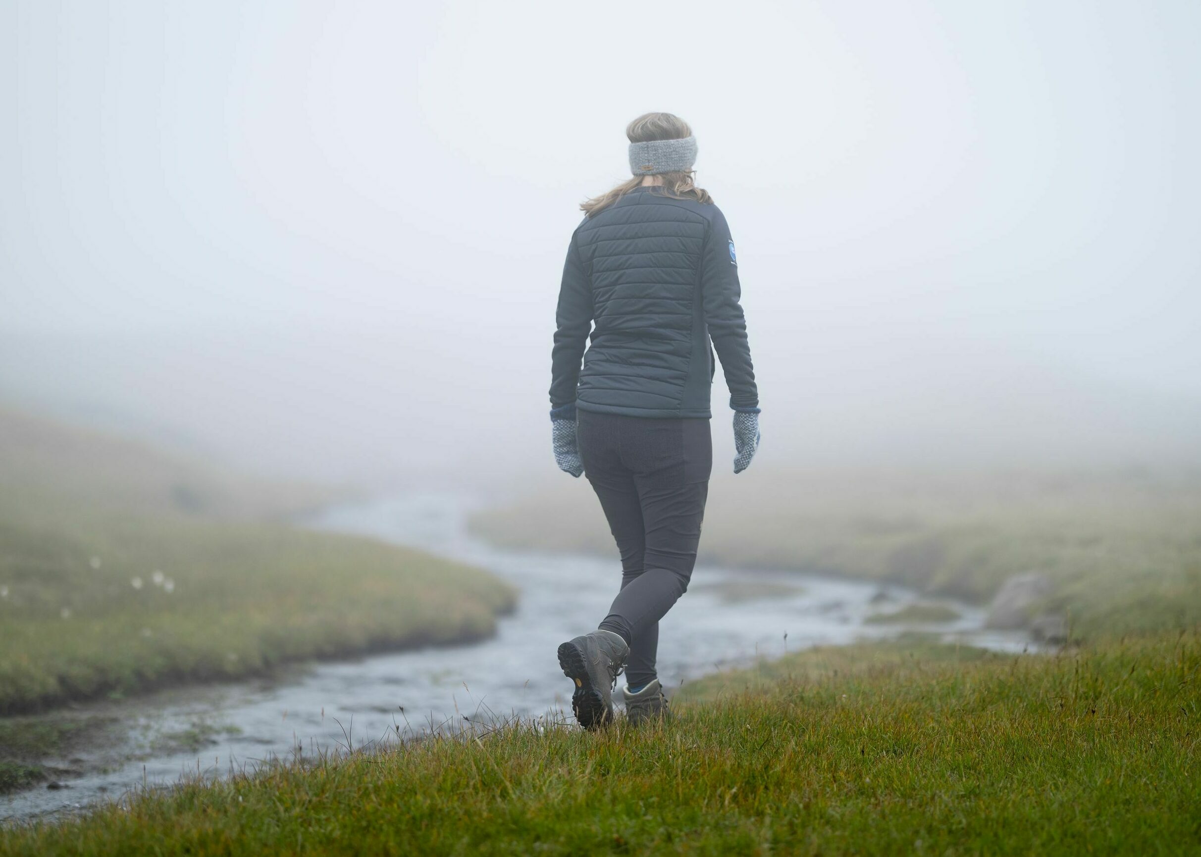 Island - Wanderin im Nebel läuft an einem Fluss entlang auf grünem Gras