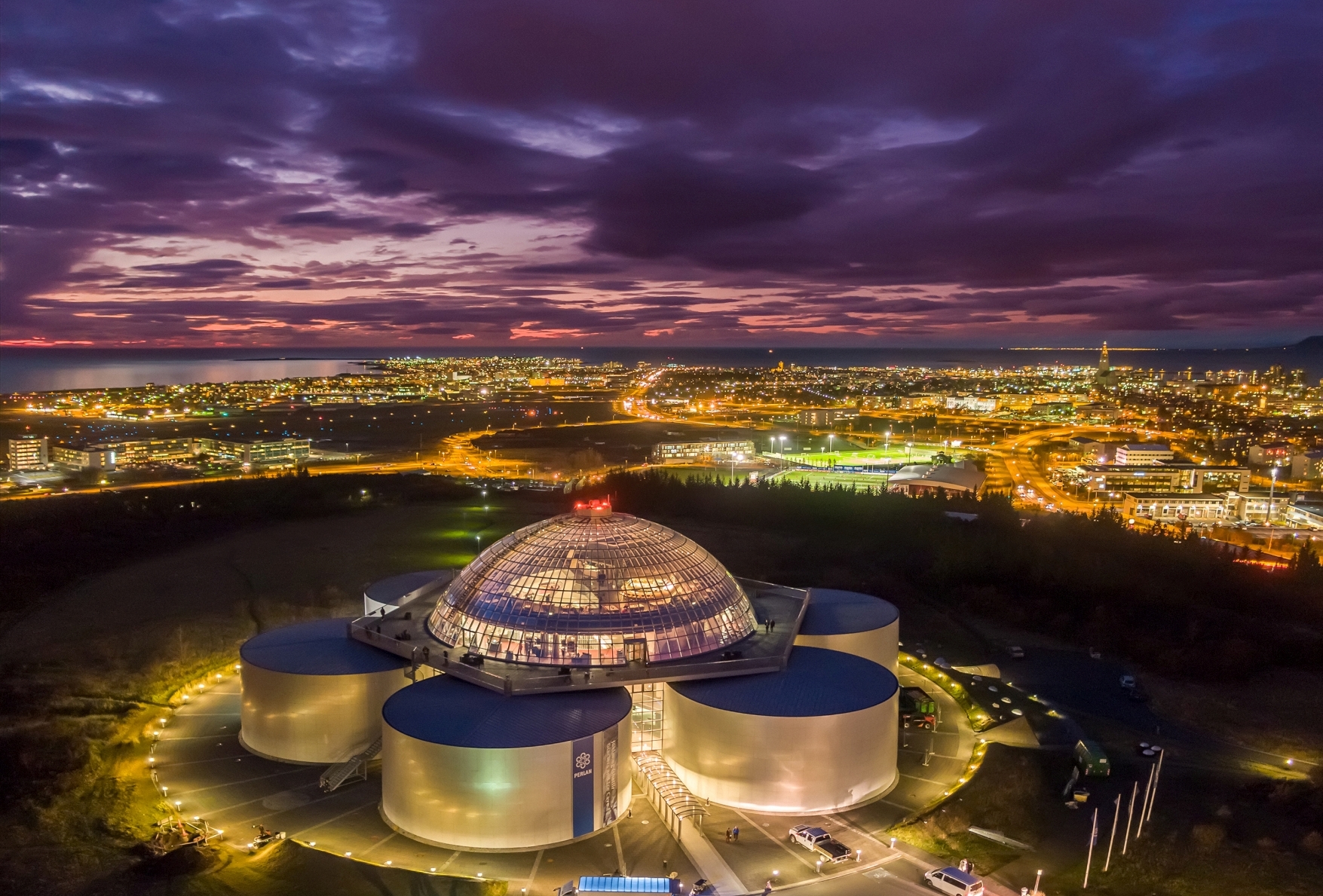 Perlan Reykjavík bei Nacht, von oben fotografiert - die Stadt im Hintergrund leuchtet, lila Himmel