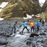 Mitglieder des Teams von Katla Travel helfen sich gegenseitig über einen Bach in Island