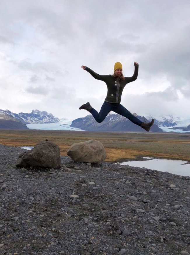 Wanderin springt vor Freude vor einem Gletscher